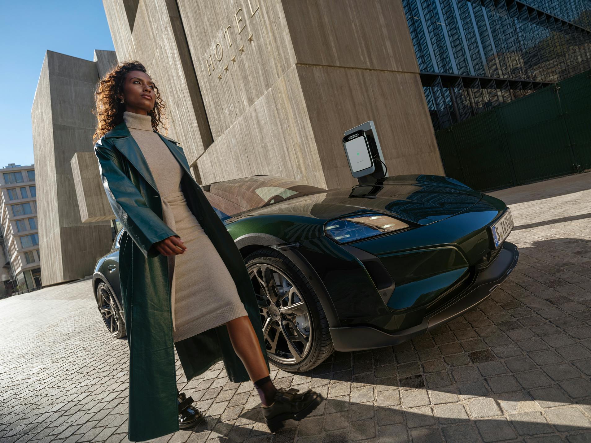 A woman wearing a coat walking past a Porsche Taycan Turbo Cross in a city.