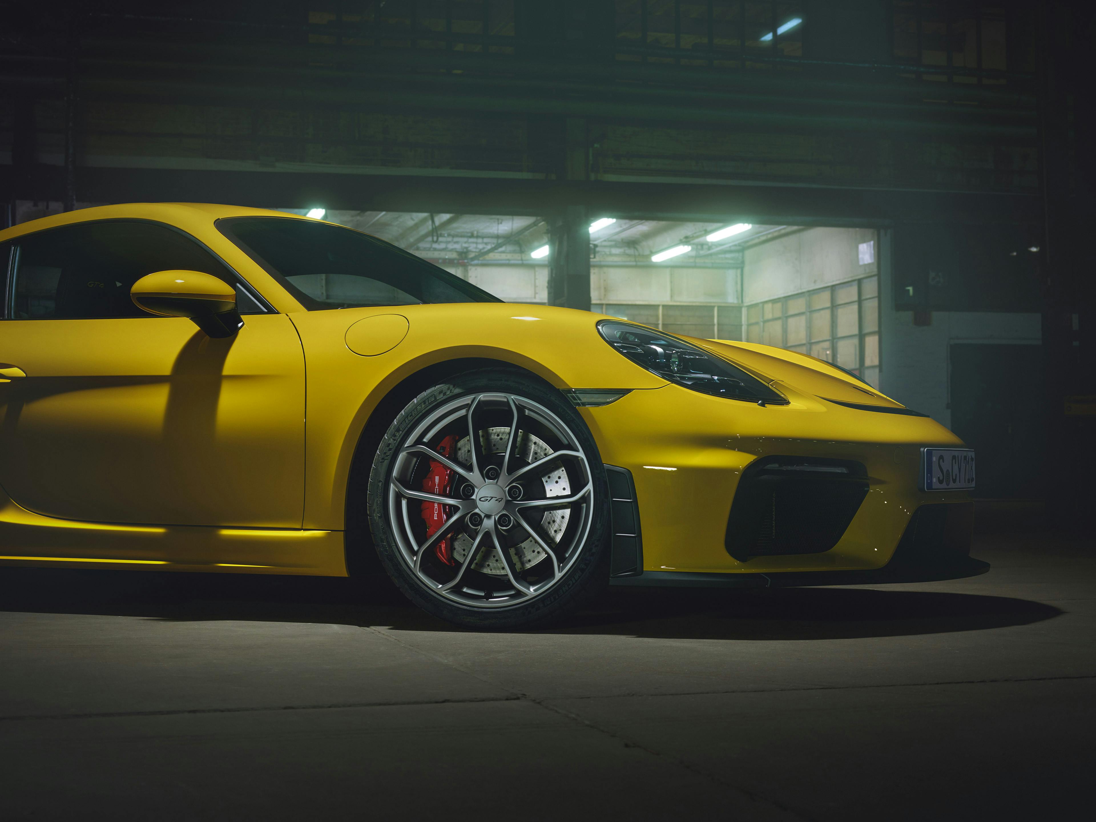 Ein gelber Porsche 718 Cayman GT4 steht in einer Tiefgarage unter dramatischem Licht.