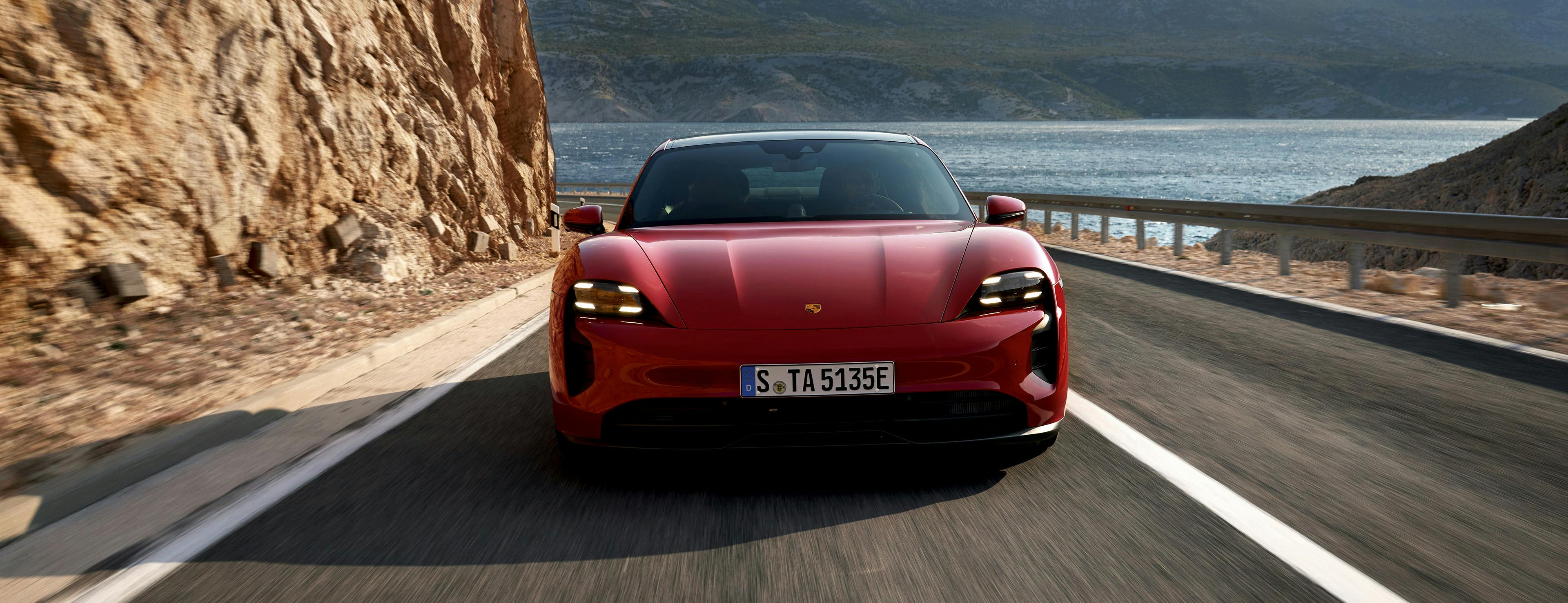 A red Porsche Taycan driving towards the camera in a maritime setting.