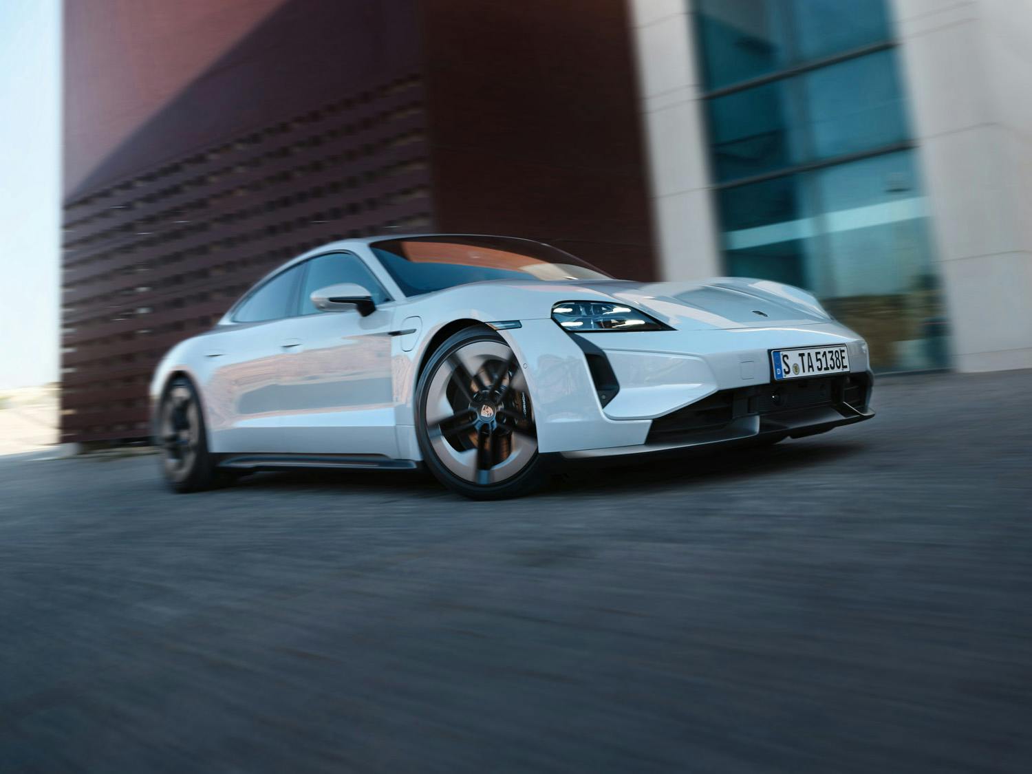Front view of a Taycan Turbo S Sport Limousine in ice grey metallic, driving in front of a building.