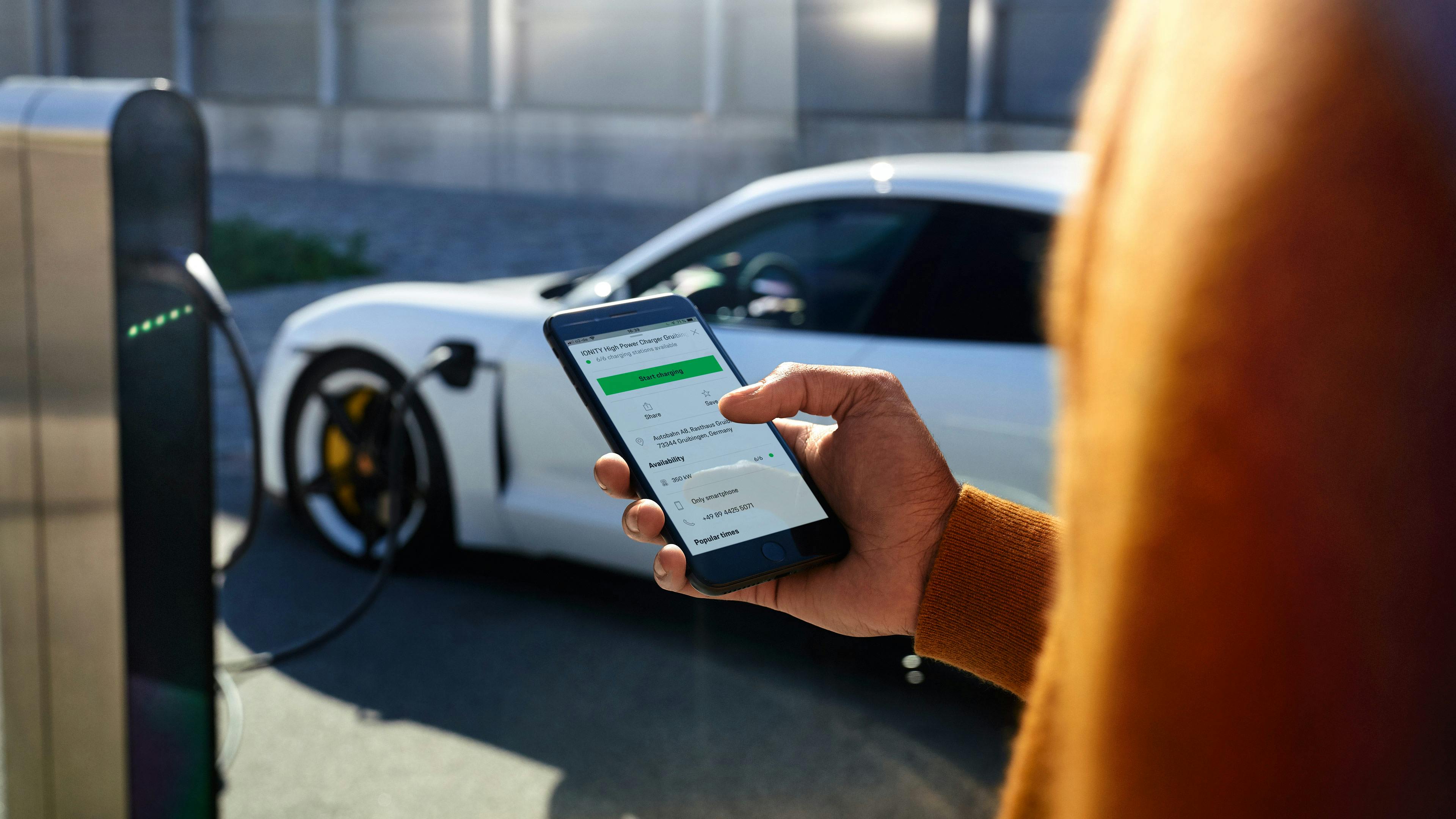 Smartphone showing Destination Charging app, with White Porsche in the background.