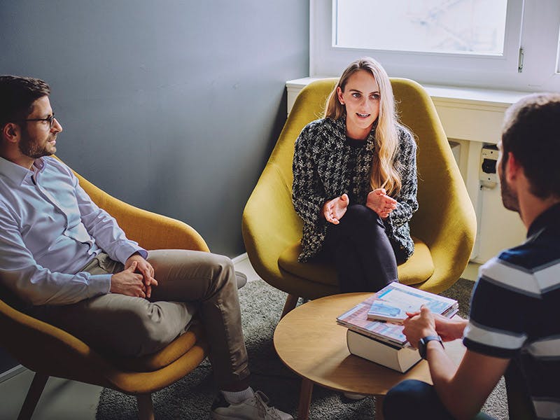 Three people are sitting around a small table talking.