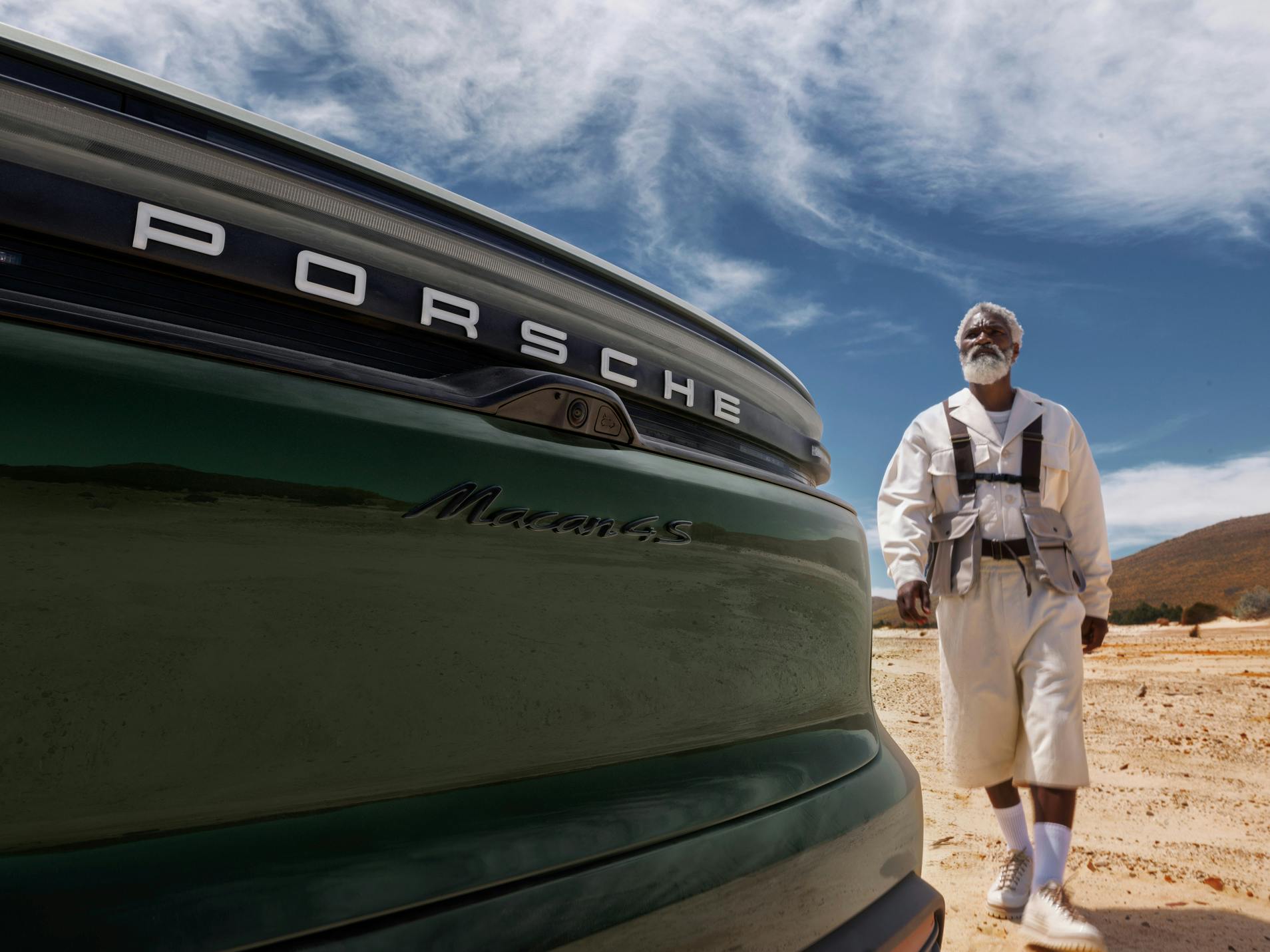Vista pormenorizada da traseira de um Porsche Macan 4S. Uma paisagem de deserto ao fundo. Um homem a caminhar em direção ao veículo.