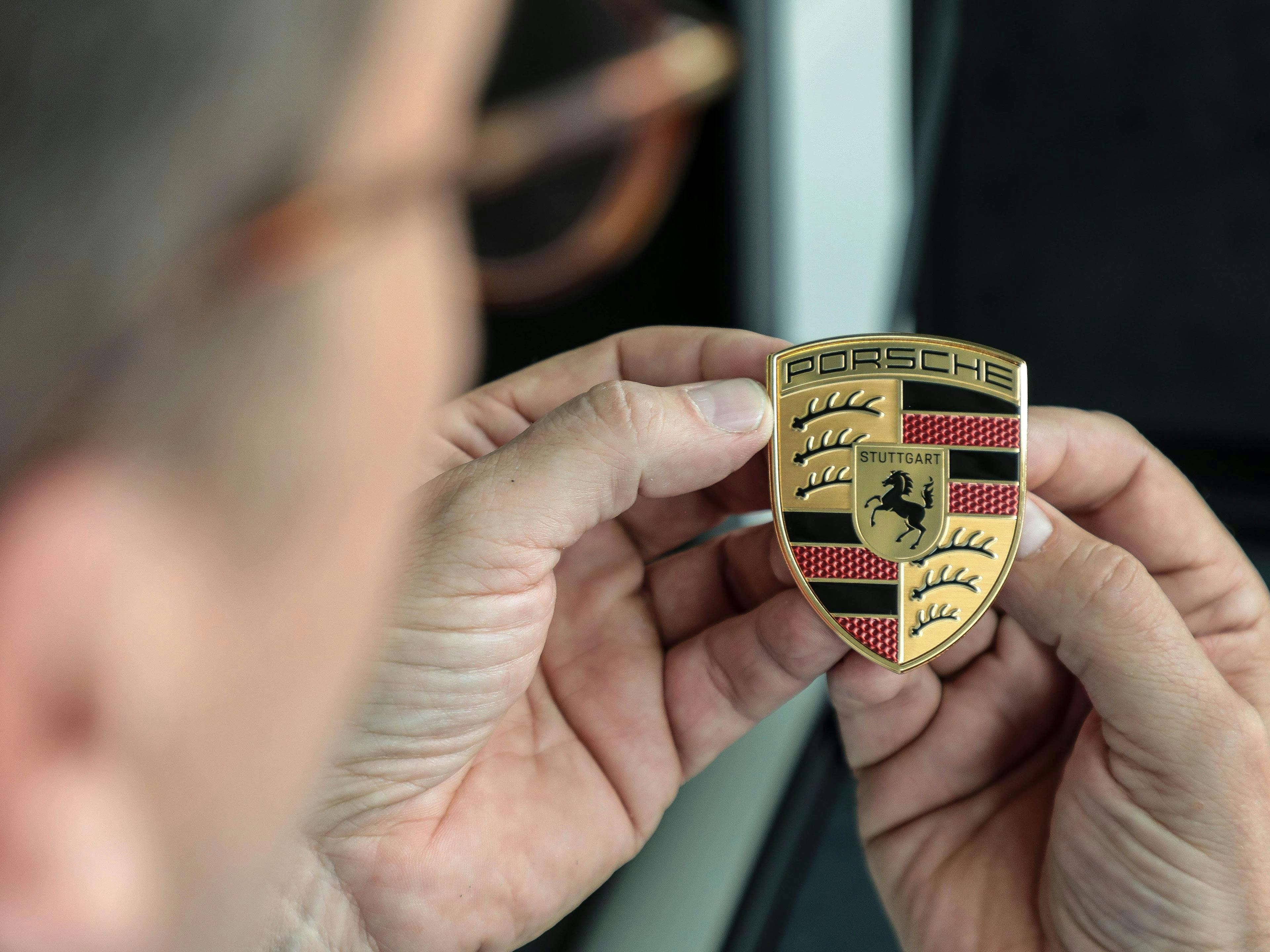 Un uomo guarda l'iconico scudo Porsche che ha tra le mani.