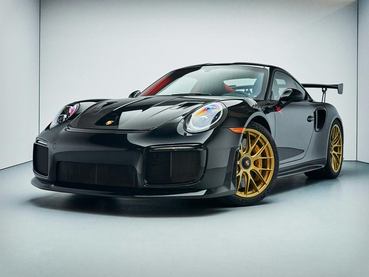 A 911 GT2 RS from the left front coloured in black with wheel rims in Pearl Gold in a PhotoBox.