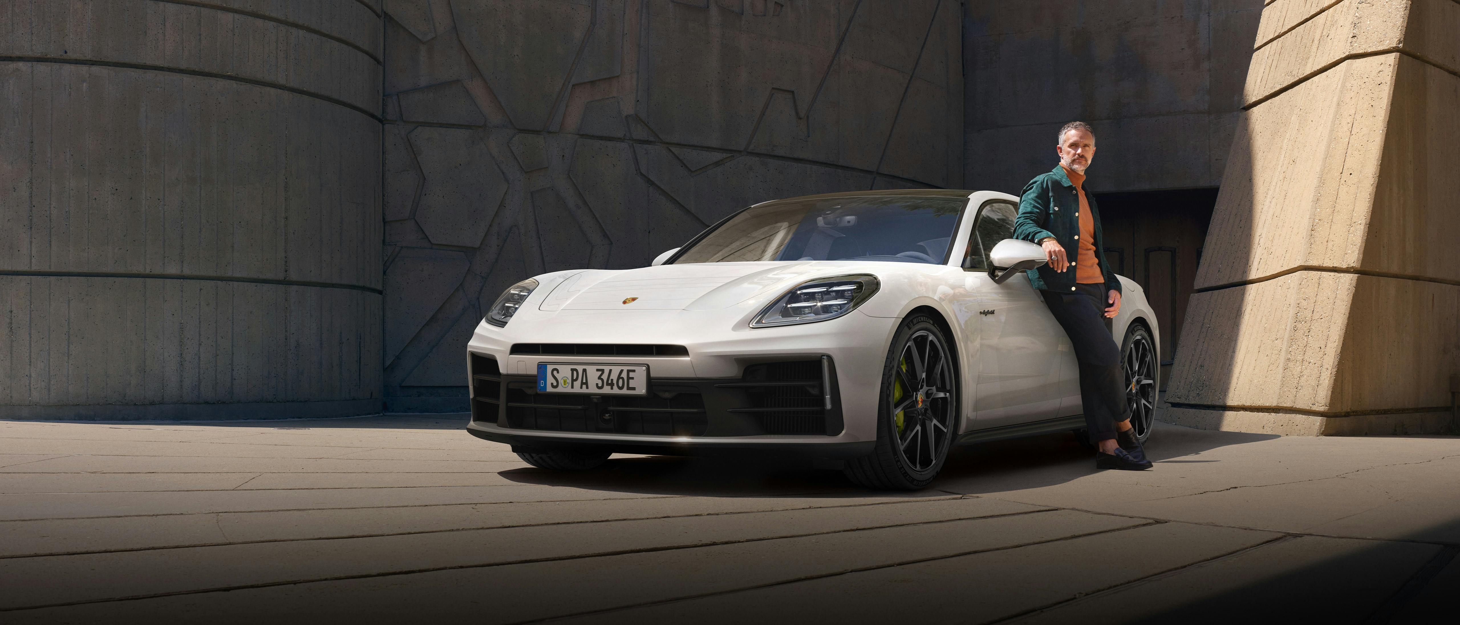 Weißer Porsche Panamera steht auf einem gepflasterten Platz, eine Person lehnt an der Fahrerseite.