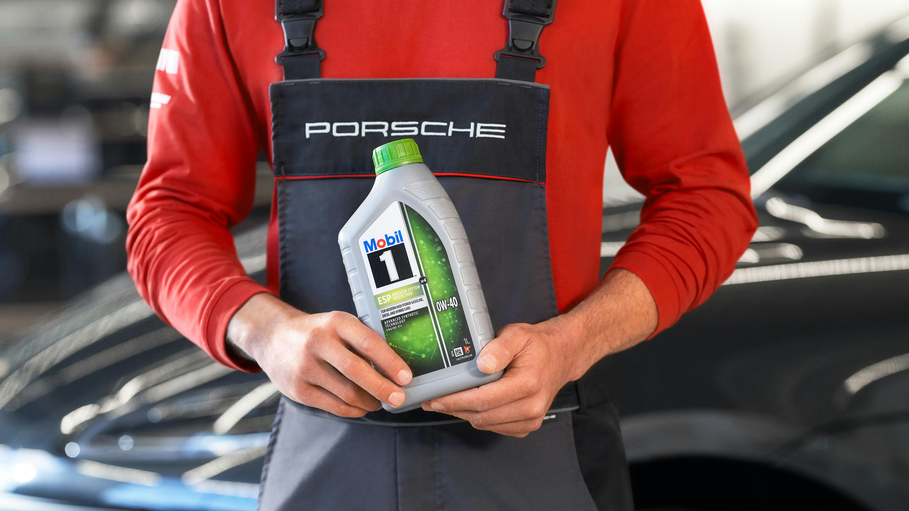 A couple and a Porsche consultant have a conversation outside a Porsche Centre. A Porsche employee and a couple are having a consultation. A Porsche can be seen in the background. In the foreground is a Mobil 1 oil bottle. A Porsche 911 can be seen in the background.