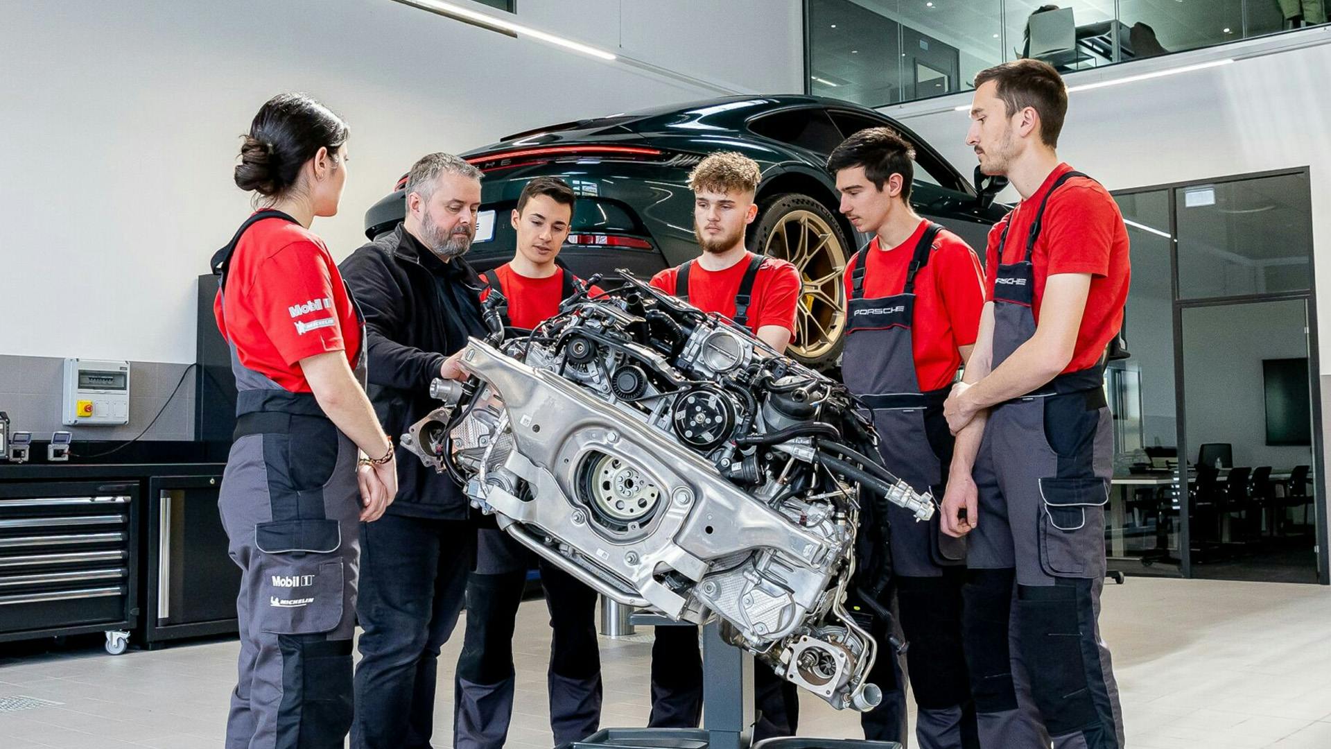 6 people observing a car's mechanical parts.