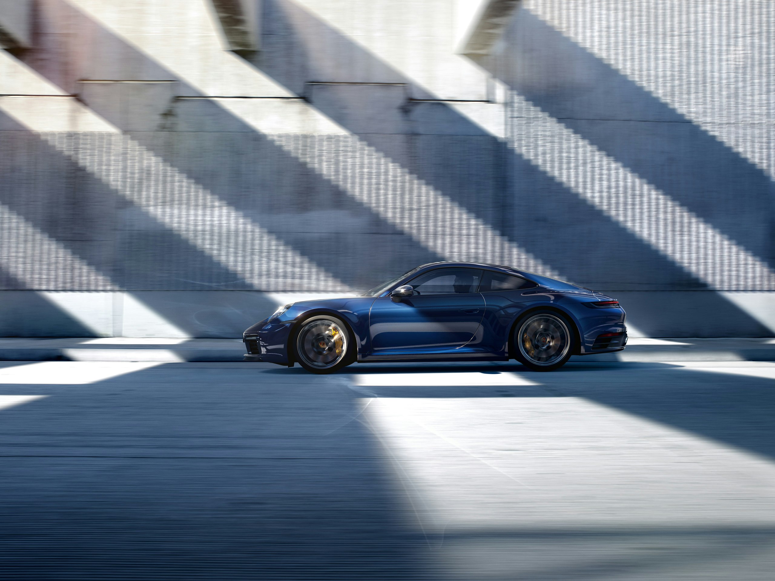 Side shot of a dark blue 911 Carrera 4S driving past a gray house facade