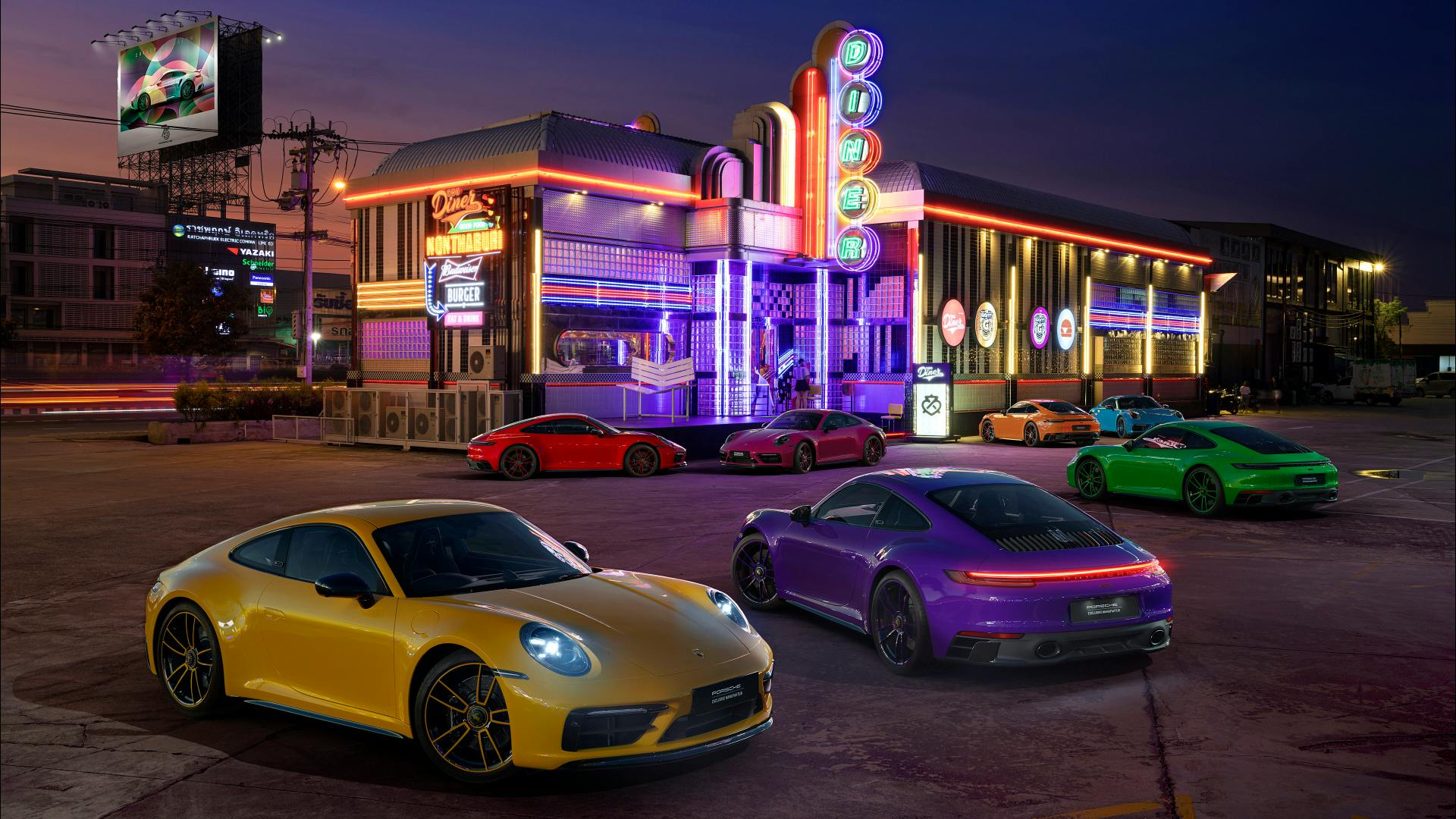 Dreams in Colours: Seven 911 models in strong different colors by night in front of an illuminated building.