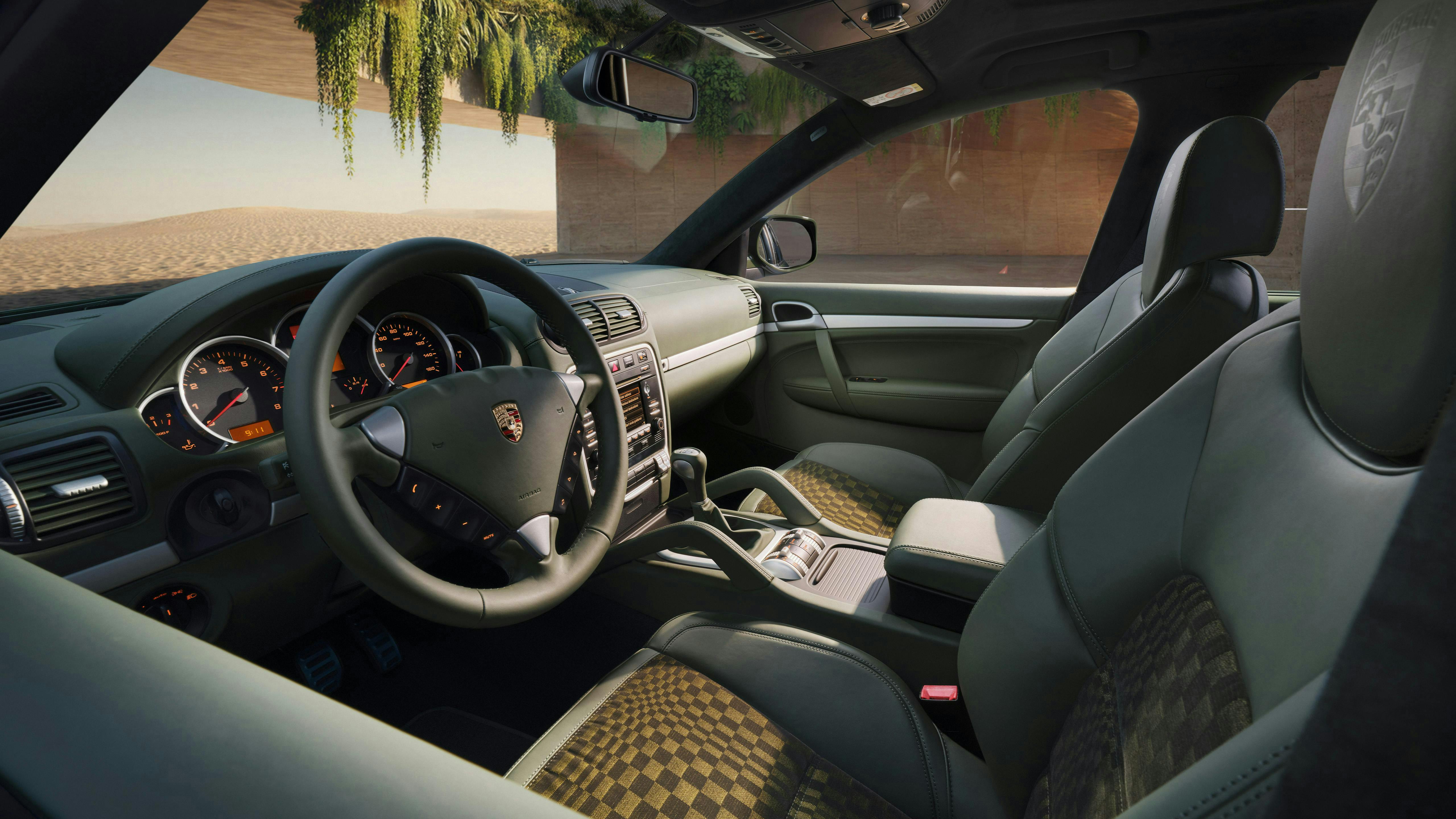 Driver’s seat perspective showing the steering wheel, center console, and Pasha black/olive upholstery inside the first-generation Cayenne GTS.