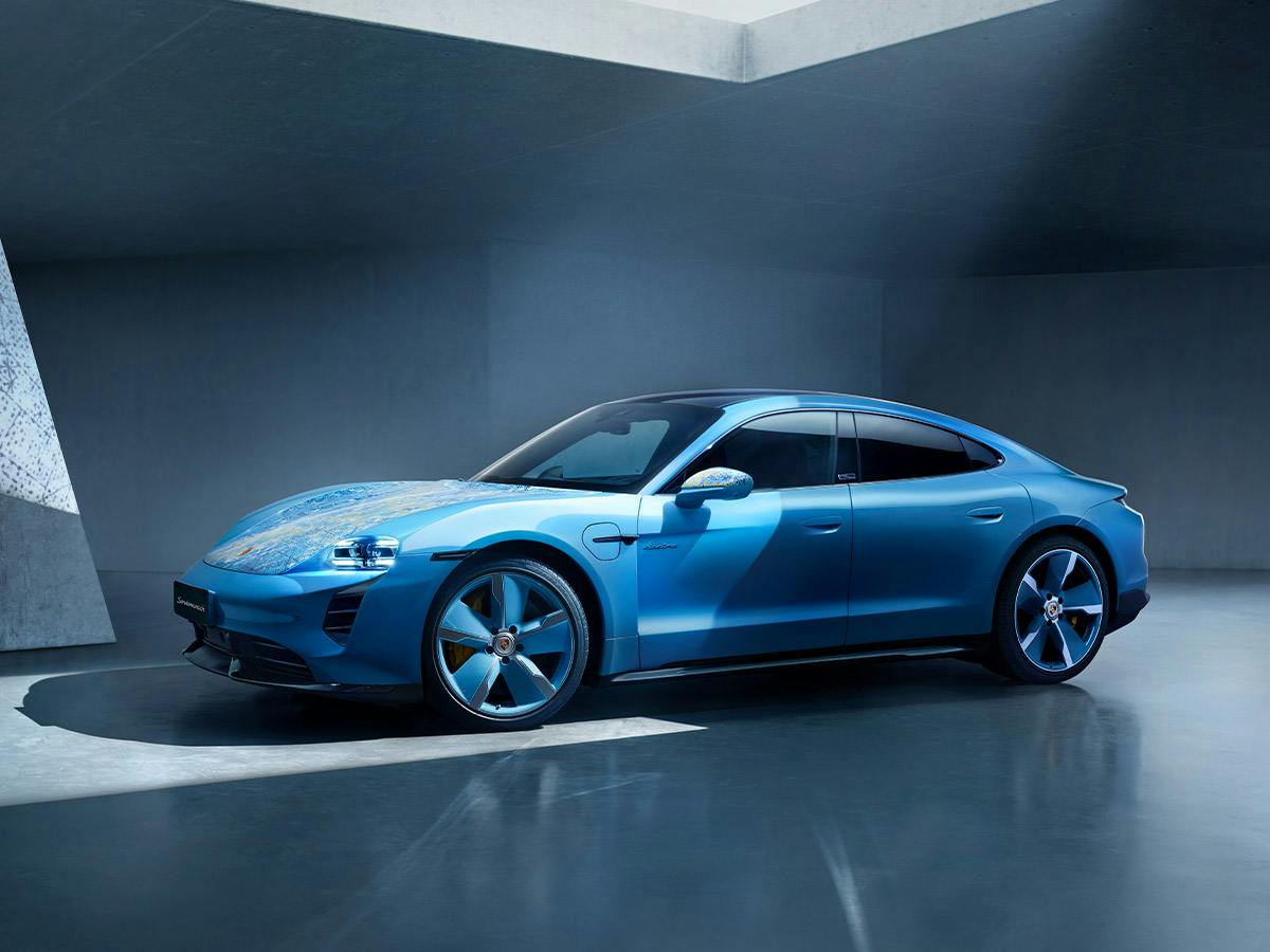 A Taycan Turbo S coloured in 914Olympblue and abstract paintings from the side in an architectural building.