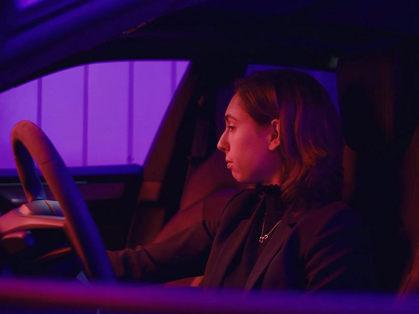 Porsche Mitarbeiterin Viktoria sitzt in einem Porsche und wird dabei in blau und rot angeleuchtet.