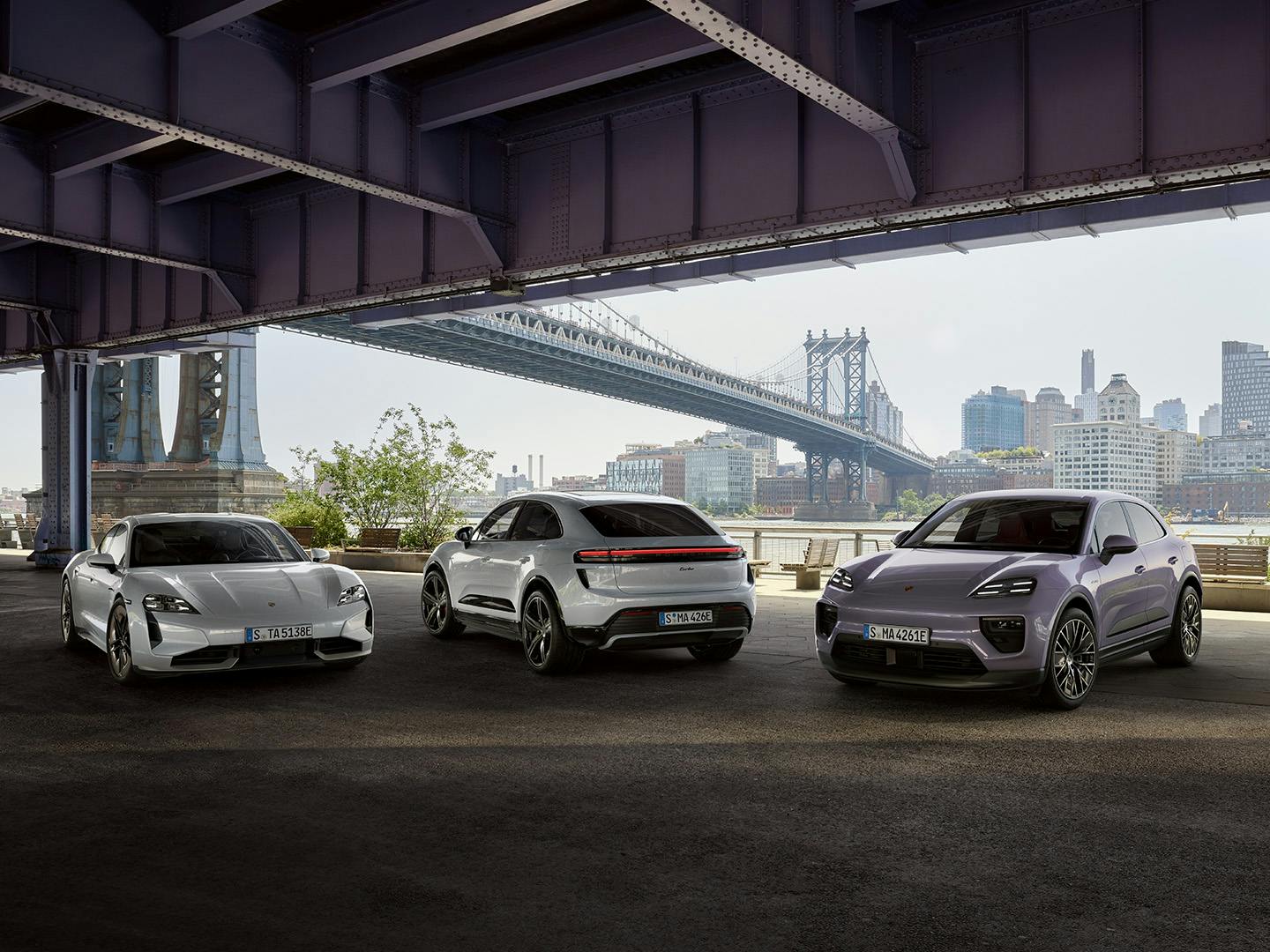 Drie porsches onder een brug met de stad op de achtergrond.
