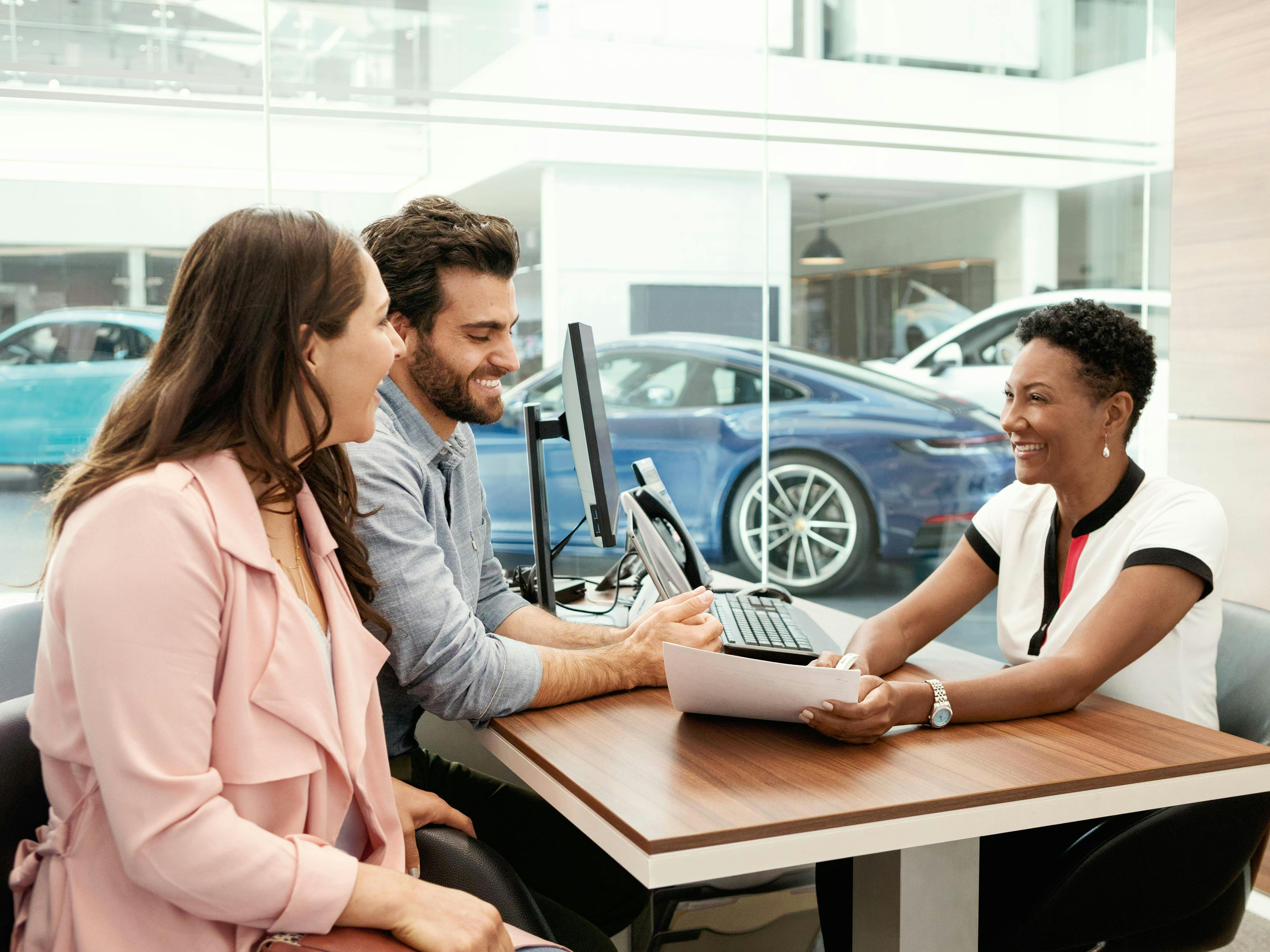 Ein Paar und eine Beraterin lächeln während einer Beratung im Porsche-Autohaus.