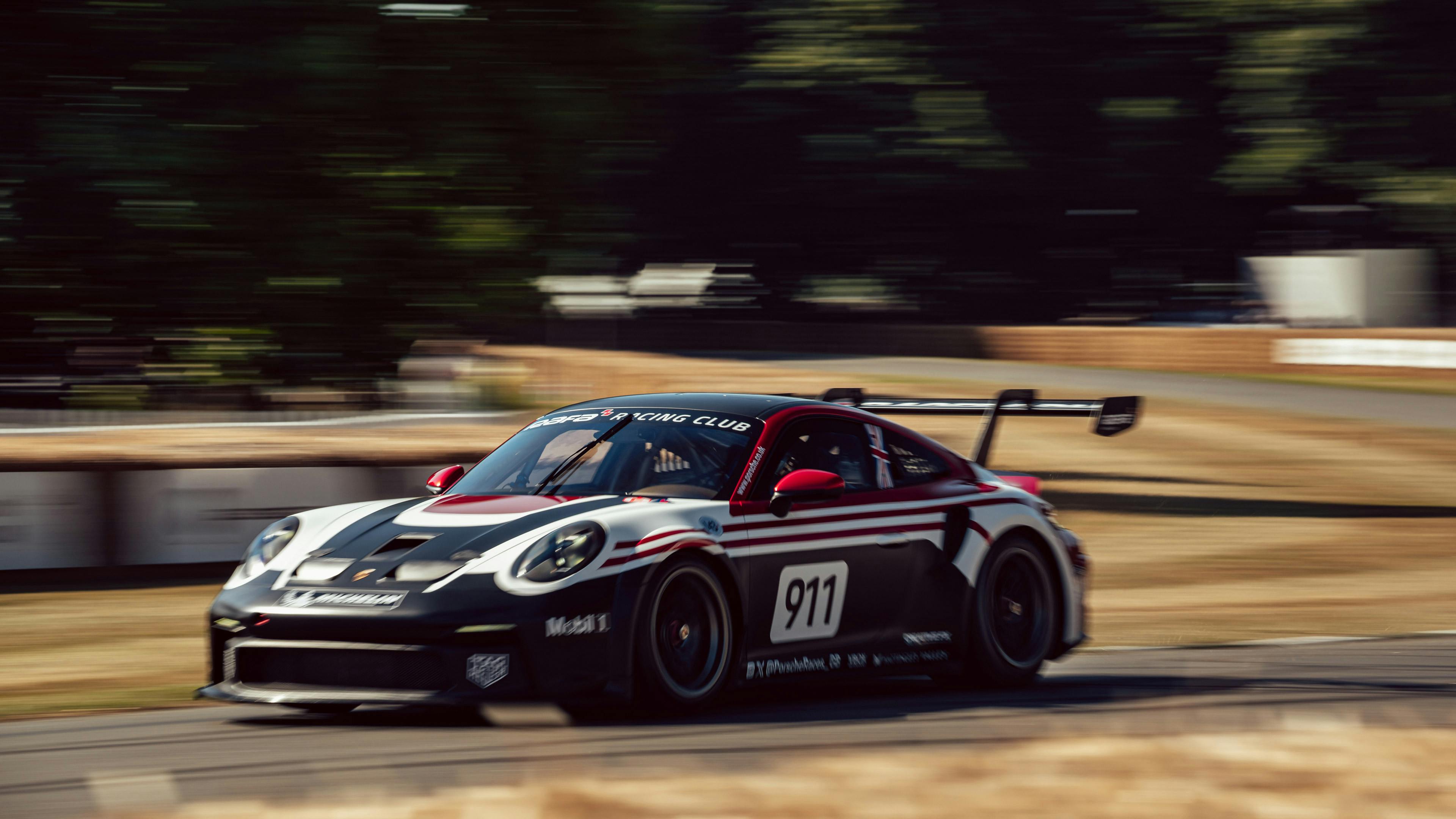 A black and white Porsche 911 GT3 Cup race car with the number 911 competing on the Goodwood hillclimb, captured at speed with a blurred green backdrop.