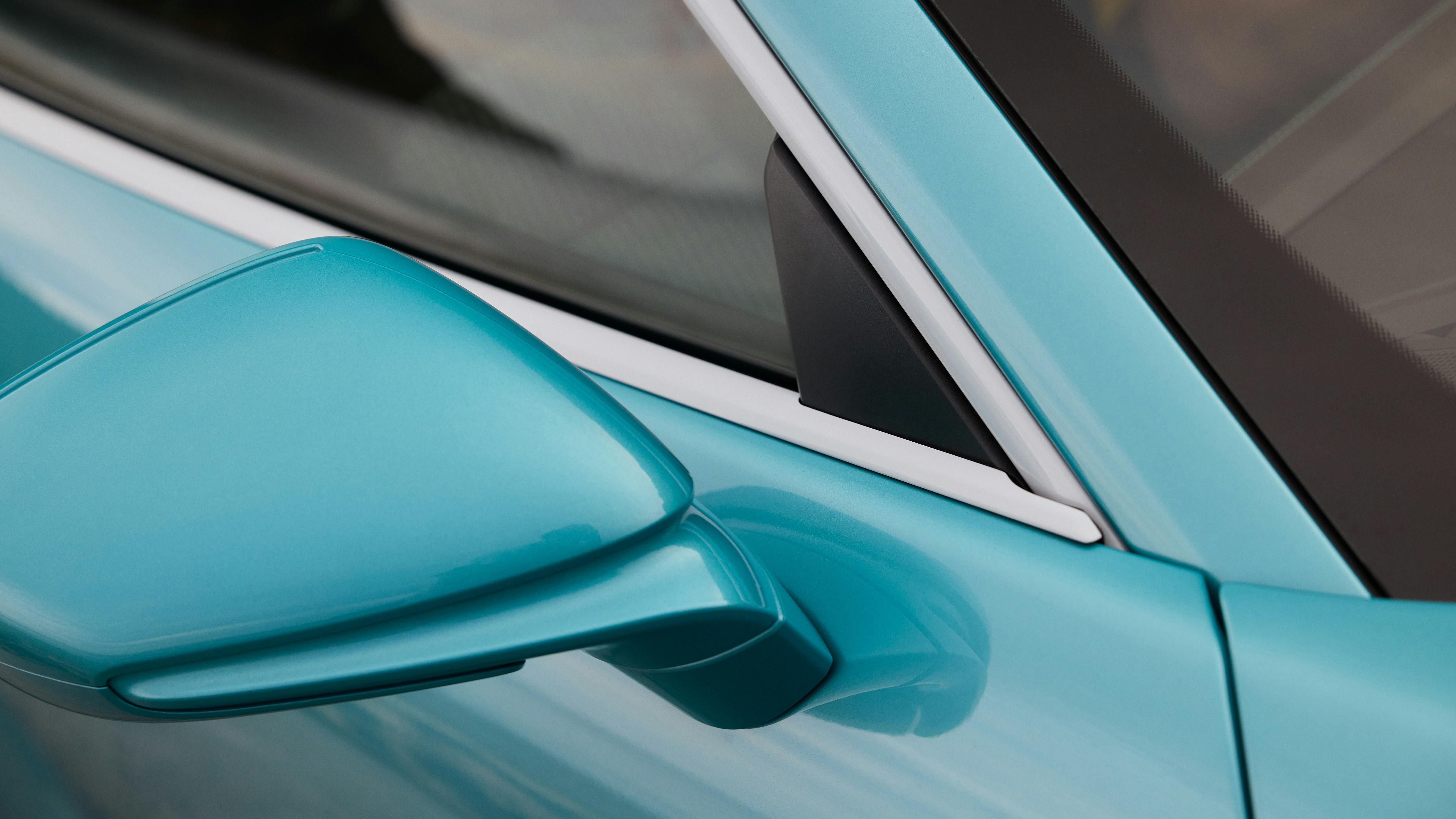 Detail of a turquoise Porsche 911 Carrera side mirror and window frame, showing smooth paint and sharp edges.