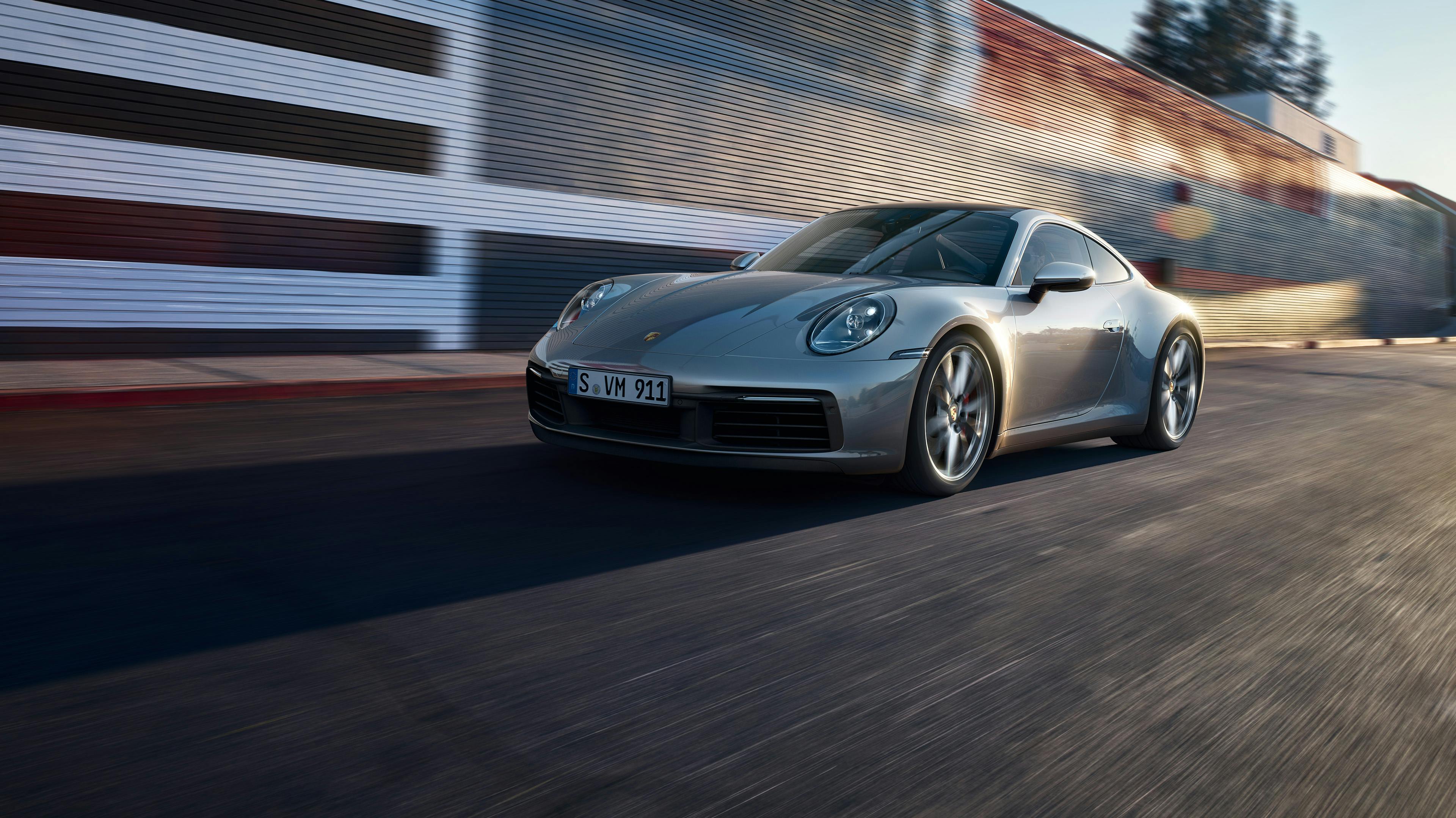 A silver Porsche 911 drives along a road.