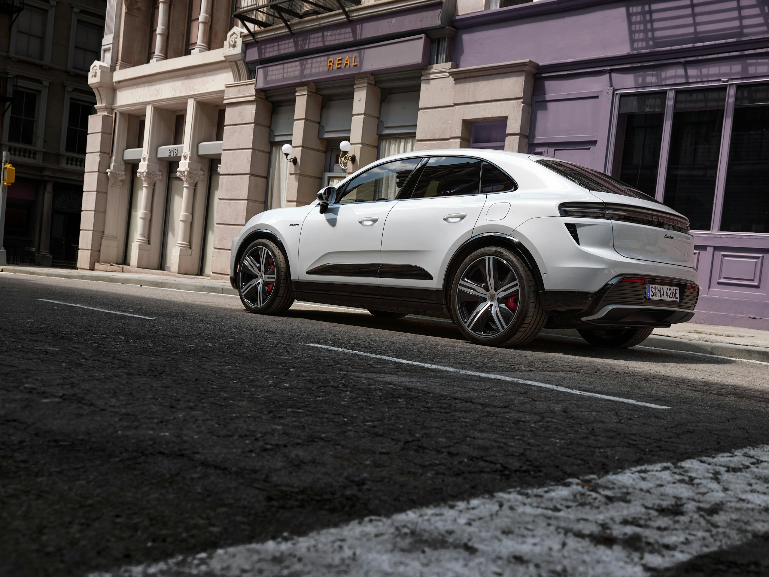Side shot of a white Macan Turbo Electric parked in front of buildings in the city.
