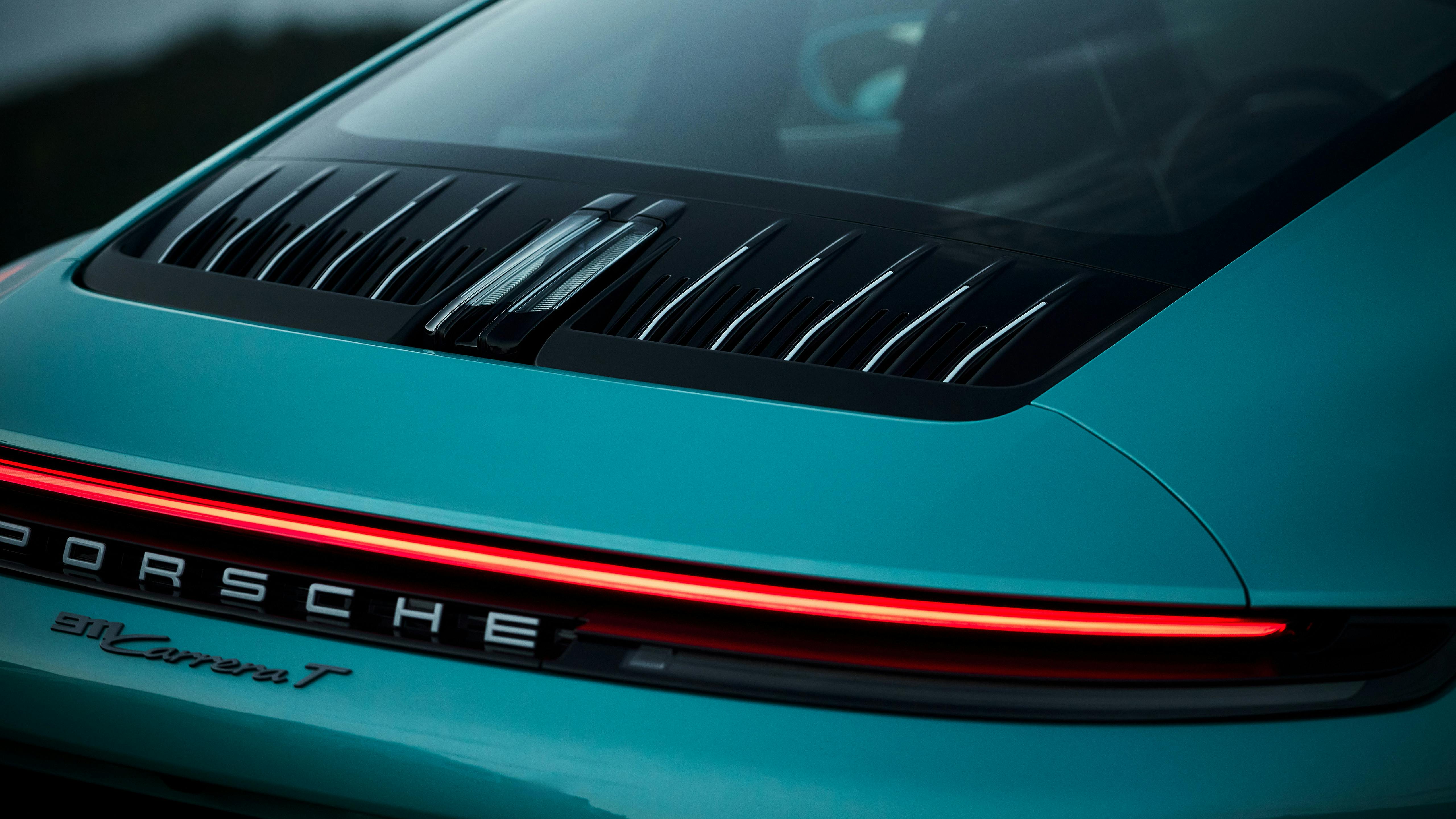 Close-up of the rear of a light blue Porsche 911 Carrera T, highlighting the illuminated red light strip, rear grille, and Porsche lettering.