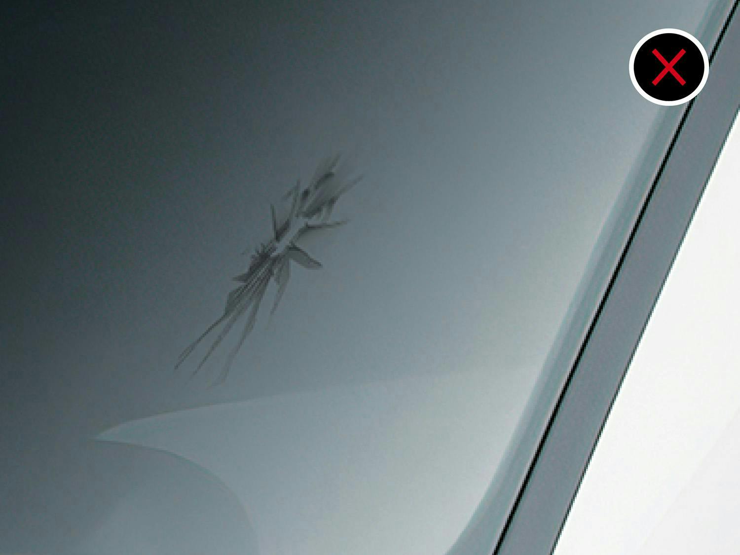 A scratched windshield surface with an X mark indicating damage.