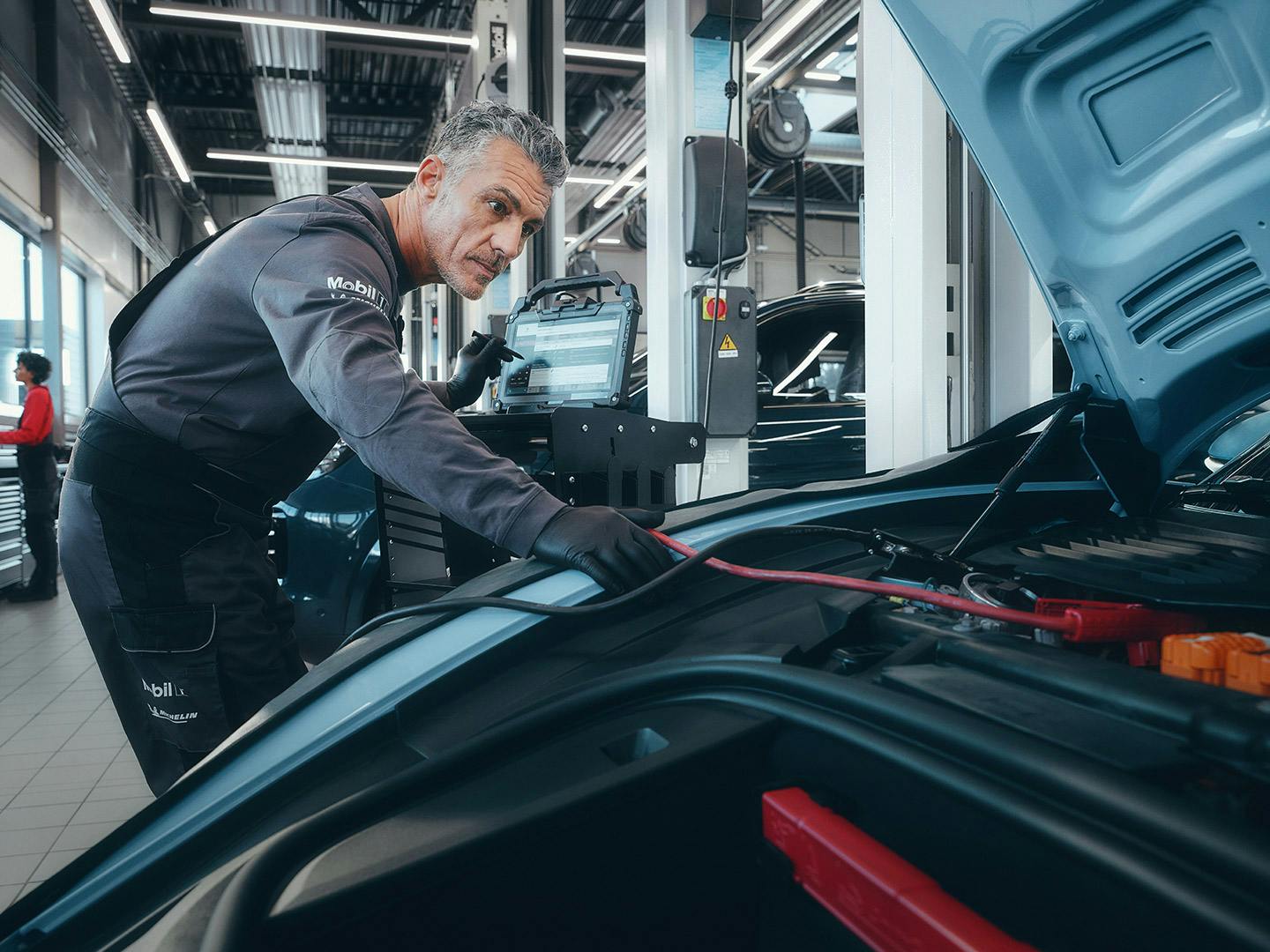 A workshop employee leaning over the open bonnet of the Taycan and using the diagnosis tester on the vehicle.