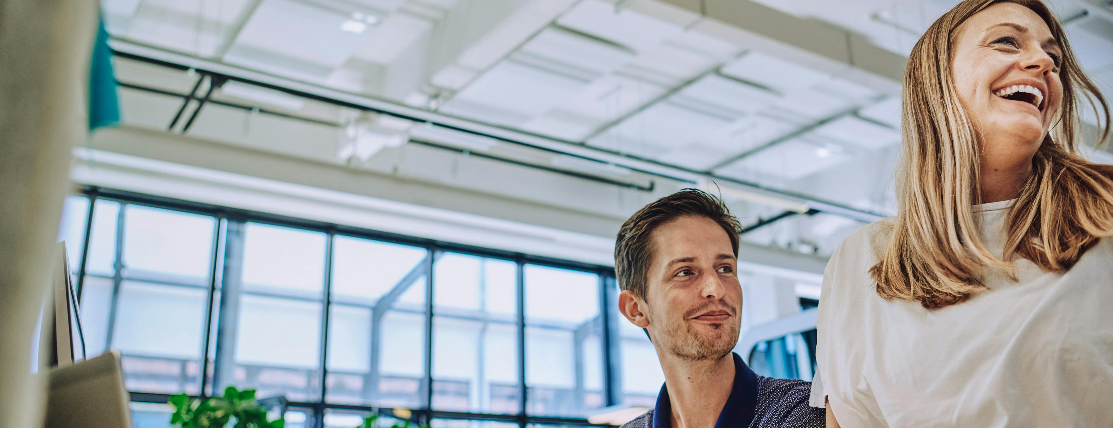 Two happy graduates at Porsche look to the side. In the background is a glass façade.