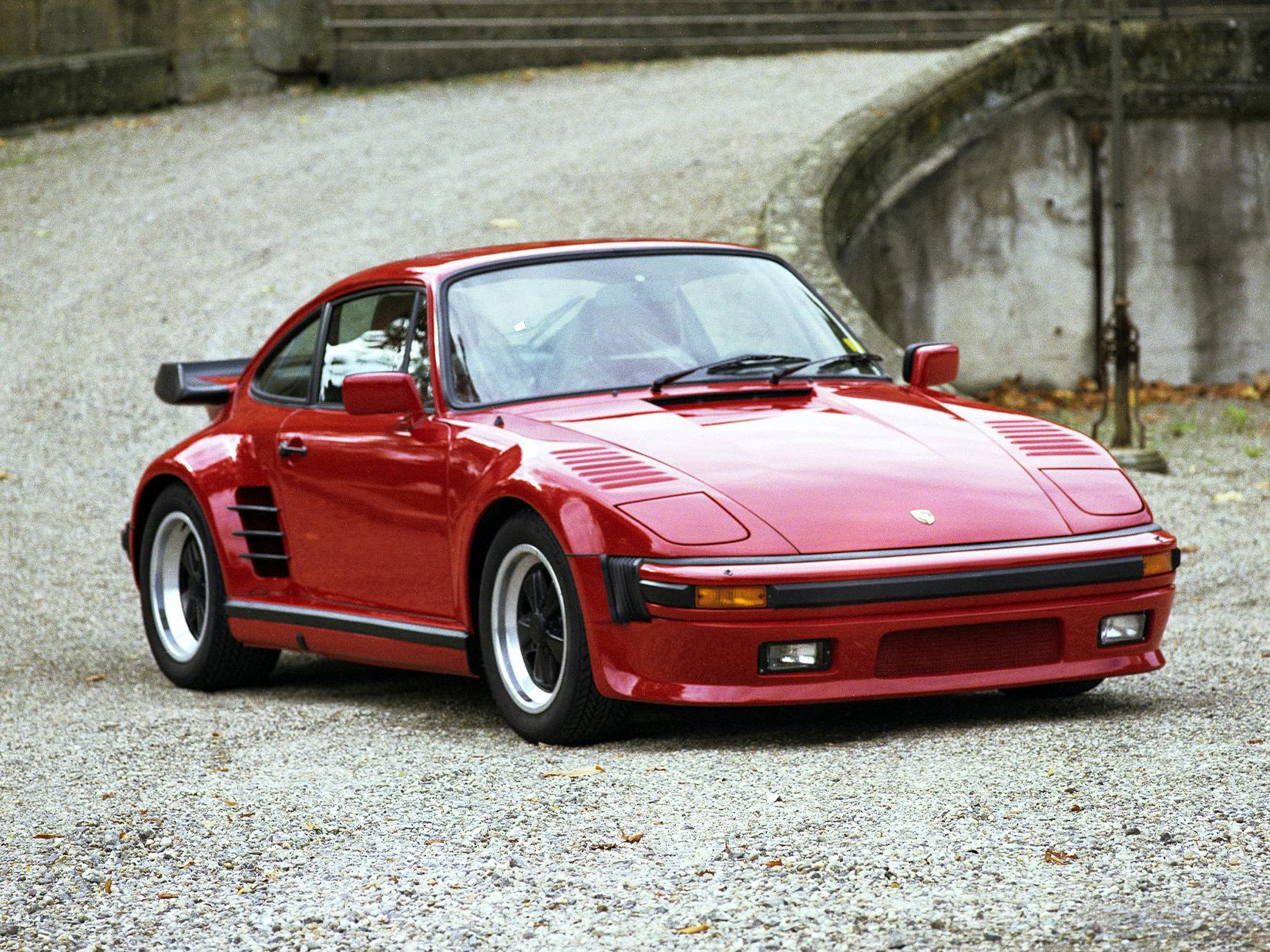 Red Porsche 911 from the 1970s, parked on a gravel path in front of a historic building.