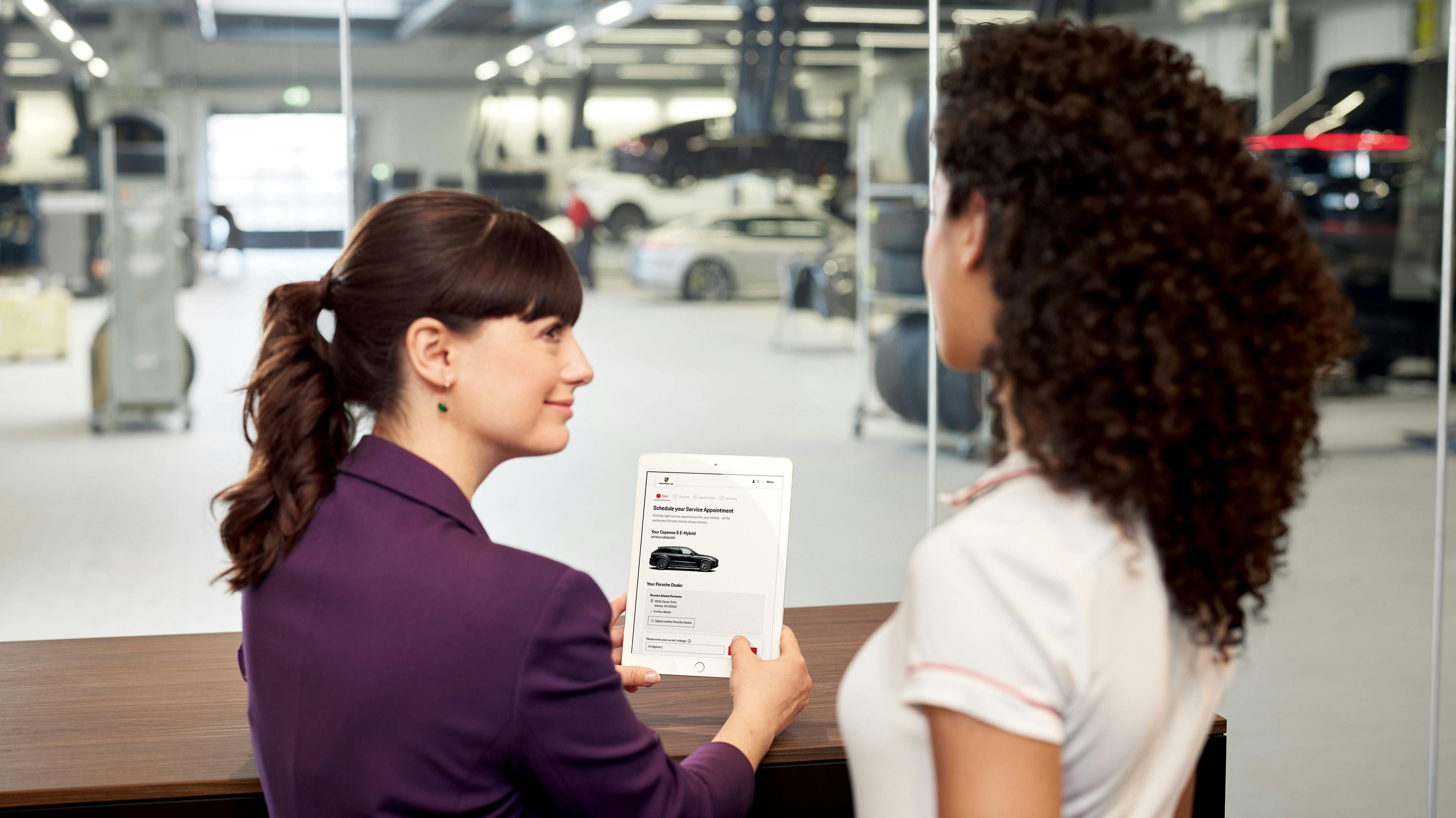 Two women review a service appointment overview on an iPad in front of the service bay.