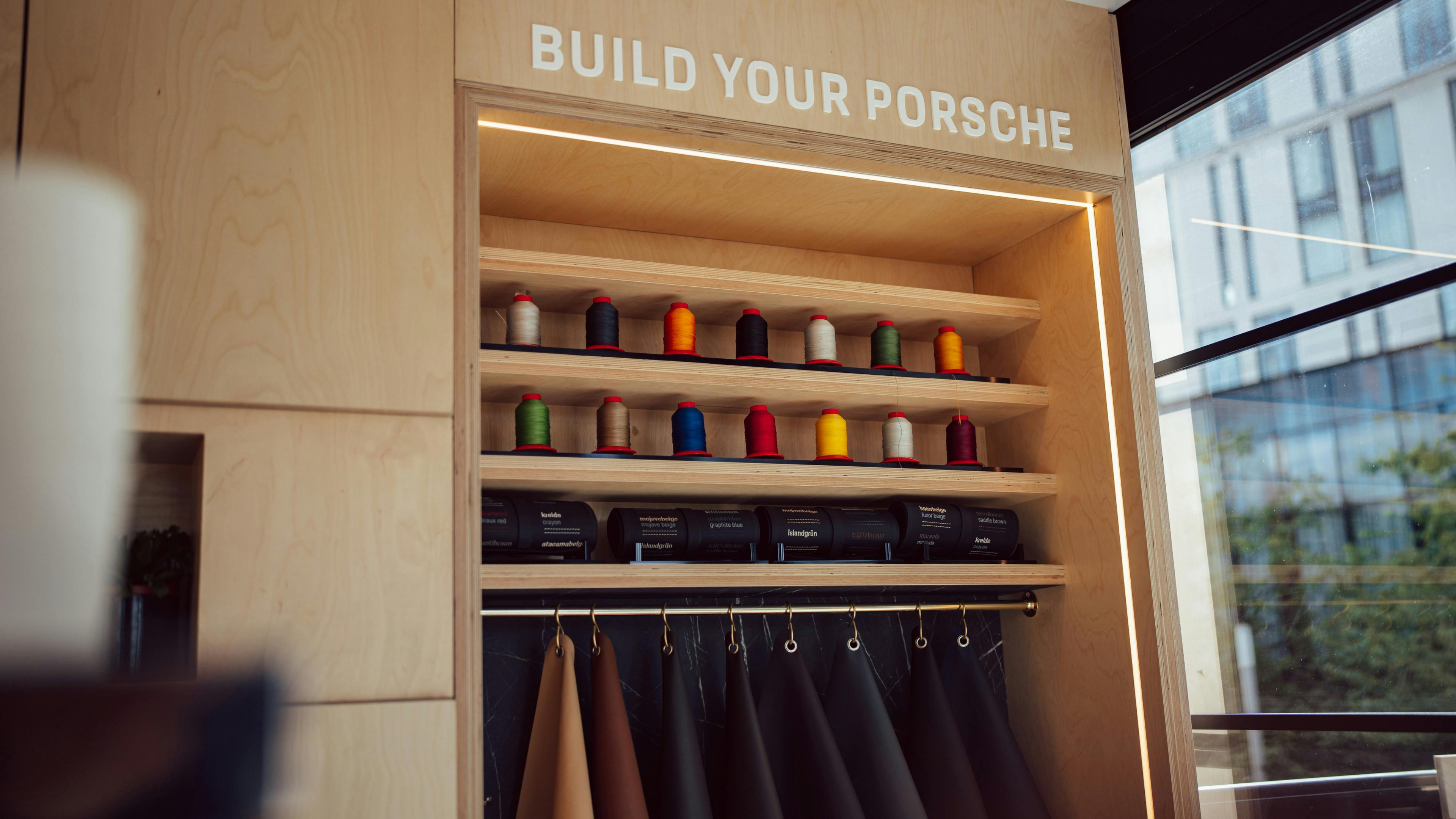 Interior display with wooden shelves labelled “Build your Porsche”, showing rows of colourful threads and hanging leather material samples.