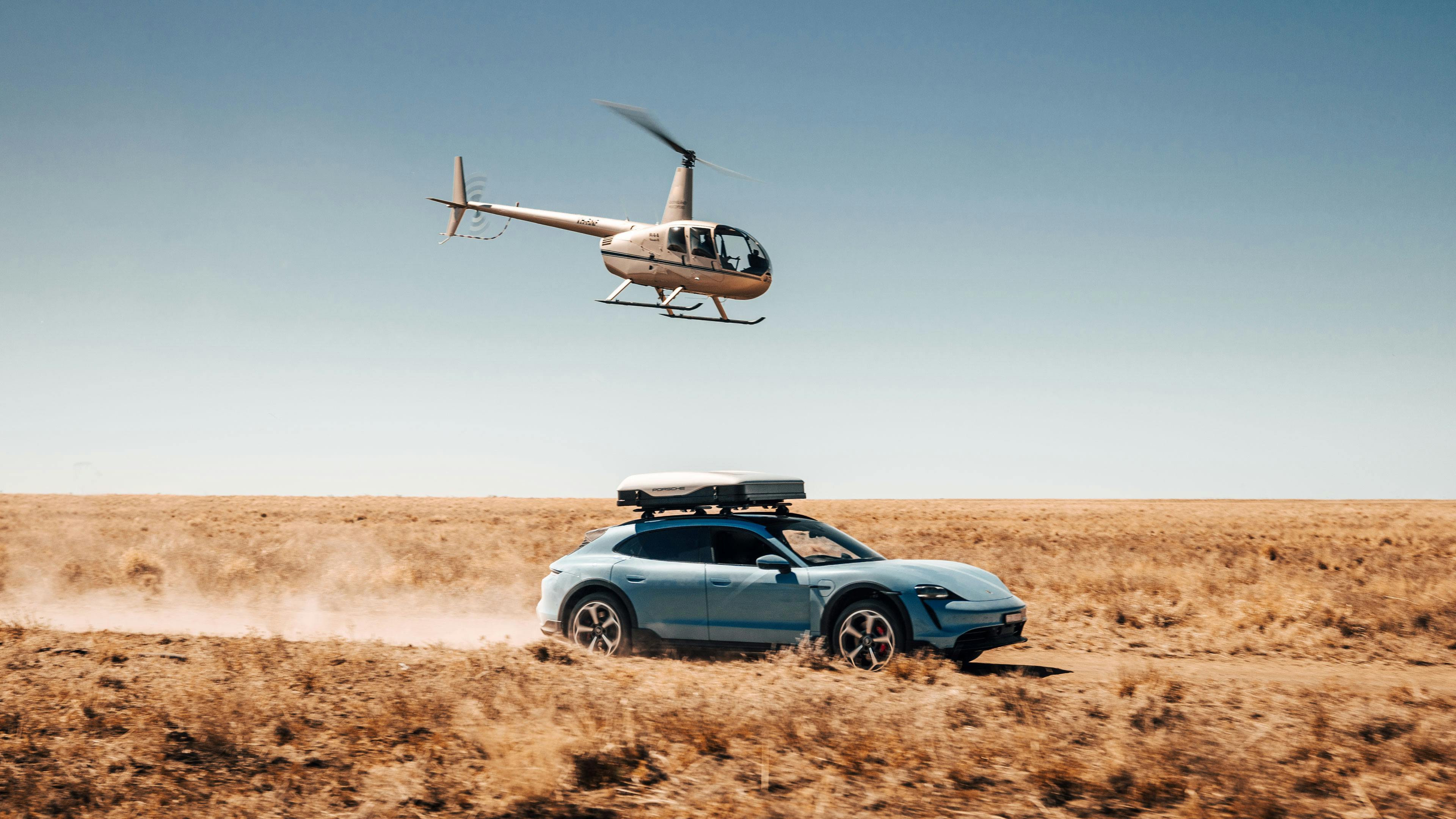 Porsche Taycan driving alongside helicopter in a desert landscape