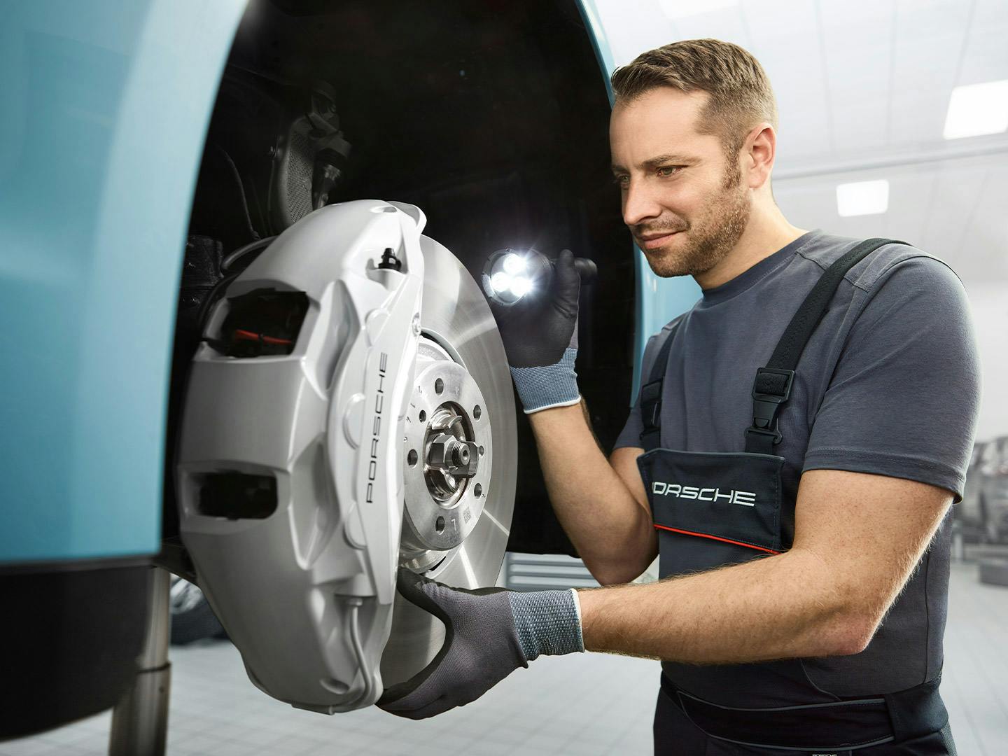 A technician inspecting the brakes on a Porsche Taycan on a lift in a modern service bay.
