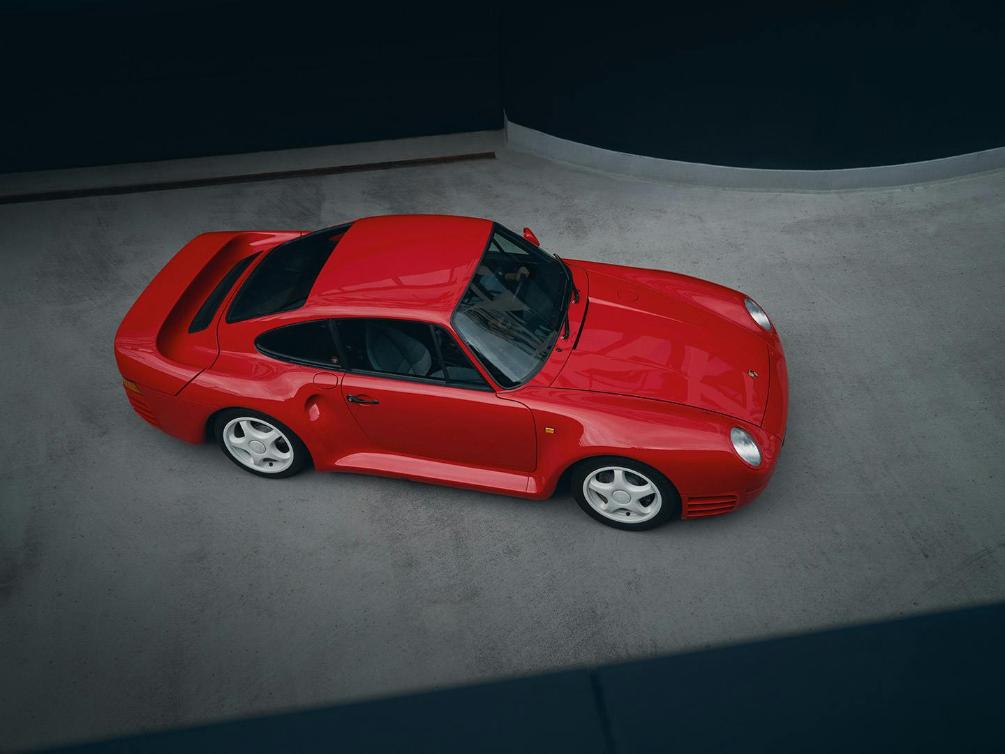 A red Porsche 959 as viewed from above in a concrete parking area.