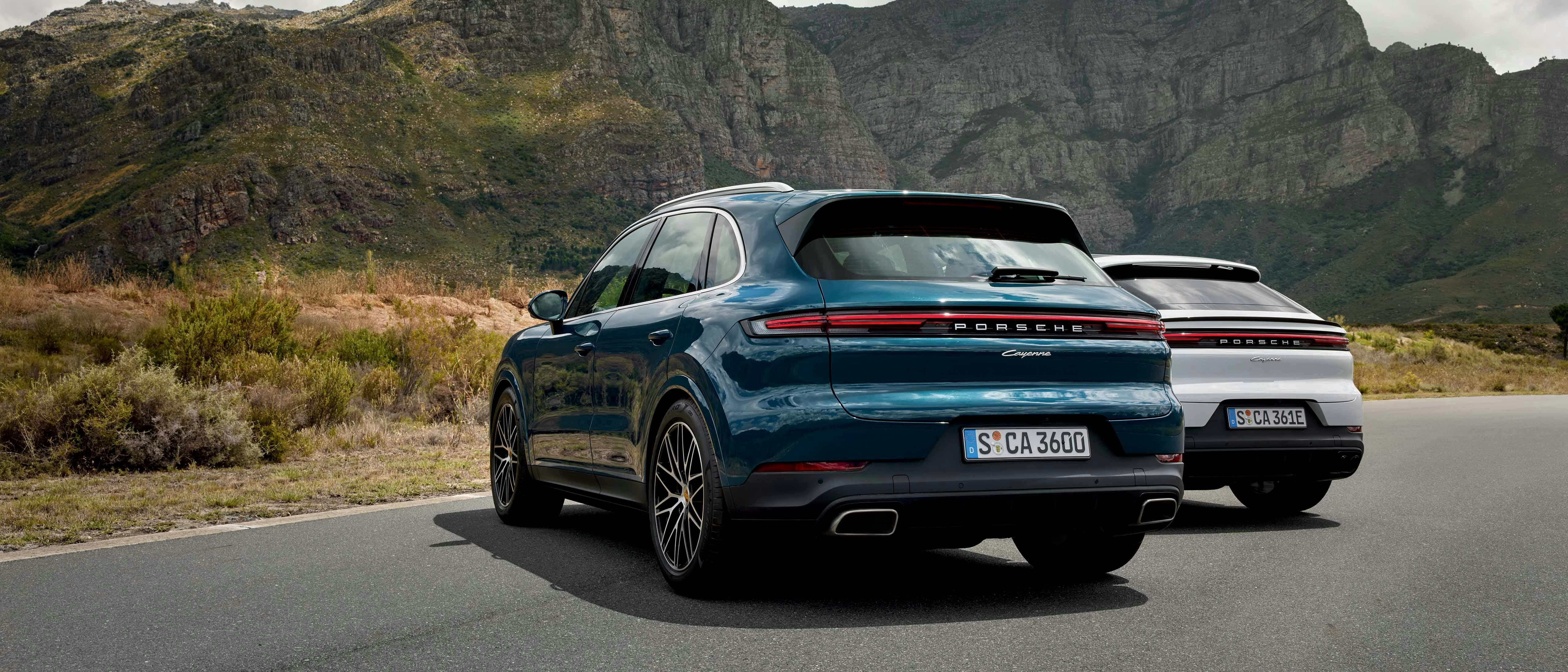 De achterkant van twee porsches die stilstaan op de weg met bergen op de achtergrond