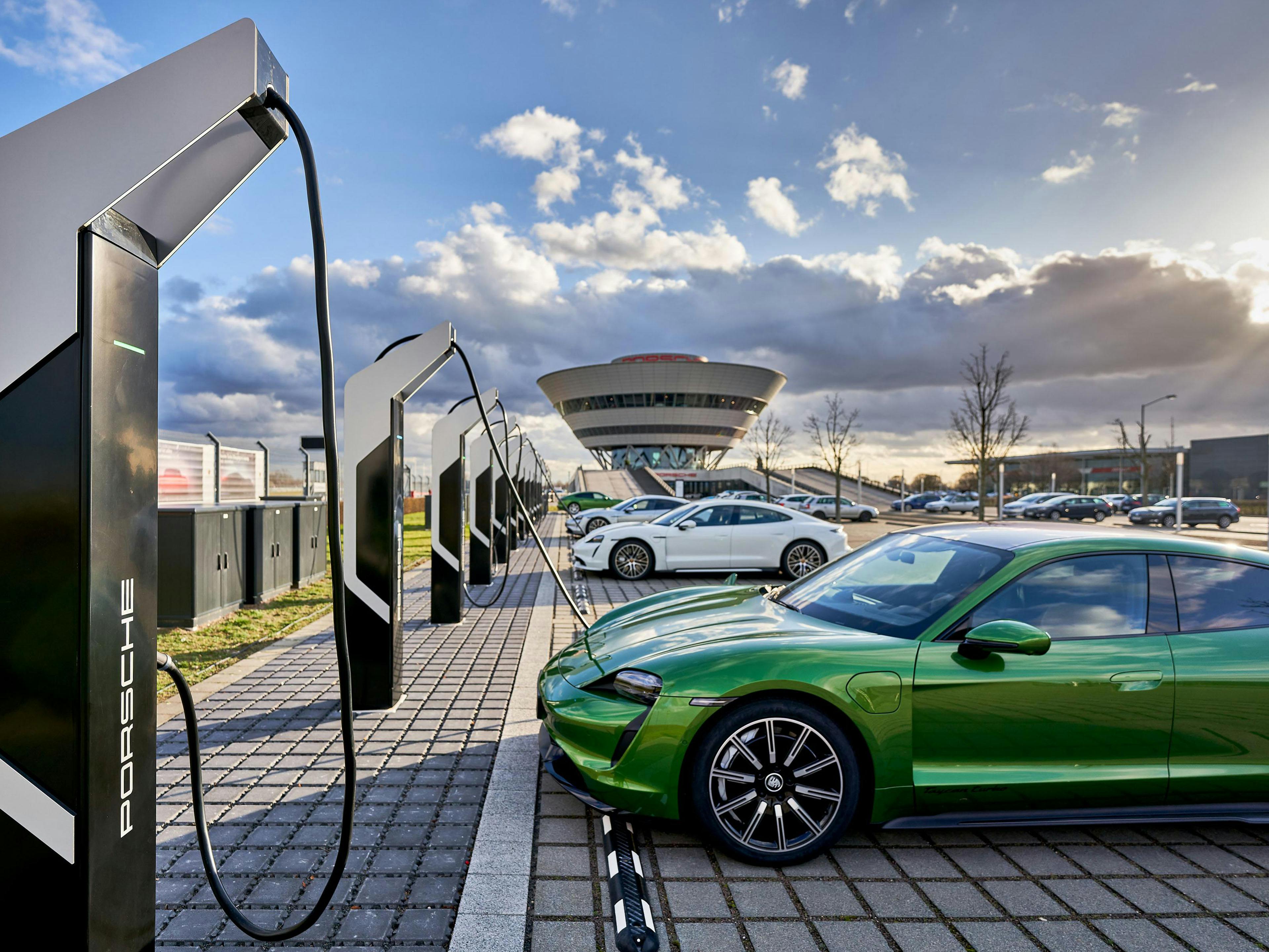 Zwei Porsche Taycan an Ladepunkten, im Hintergrund das Porsche Experience Center Leipzig.