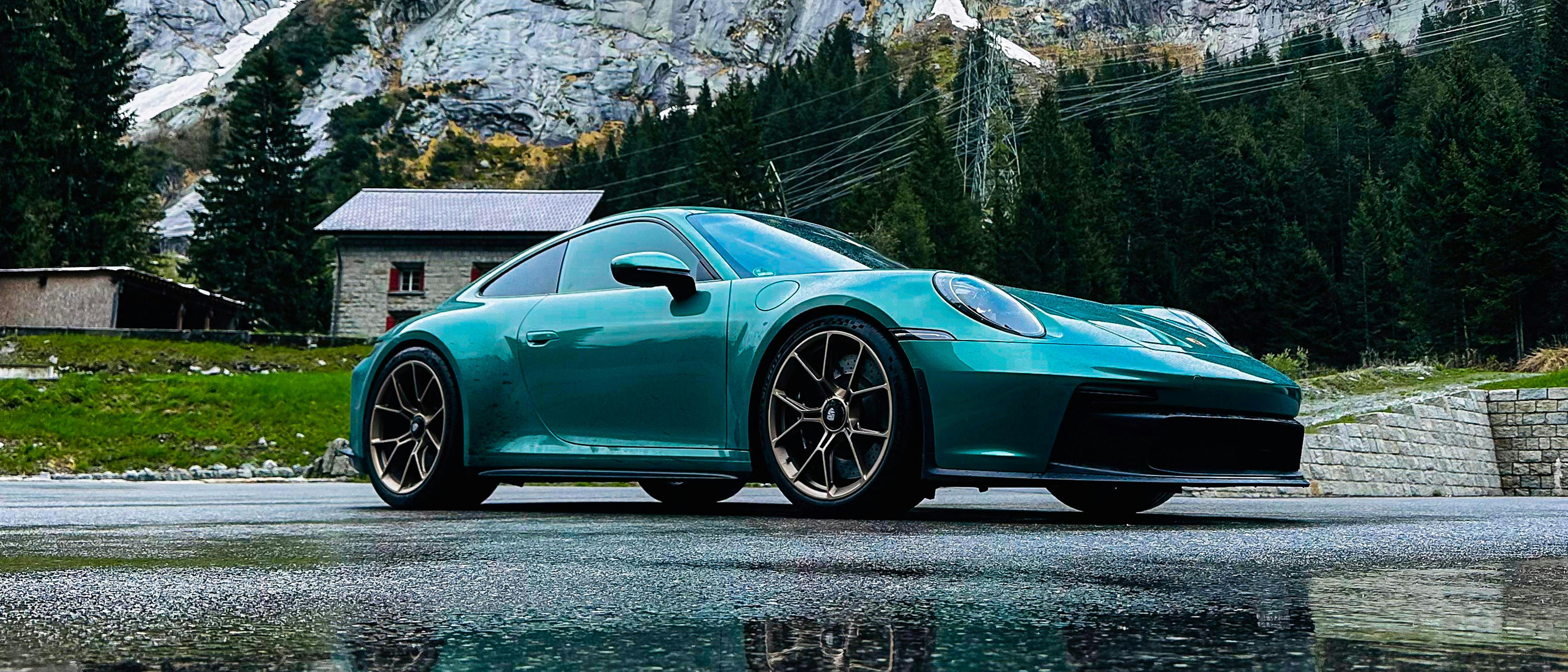 A 911 GT3 Touring in individual colour Racing Green Metallic on a road in the mountains.