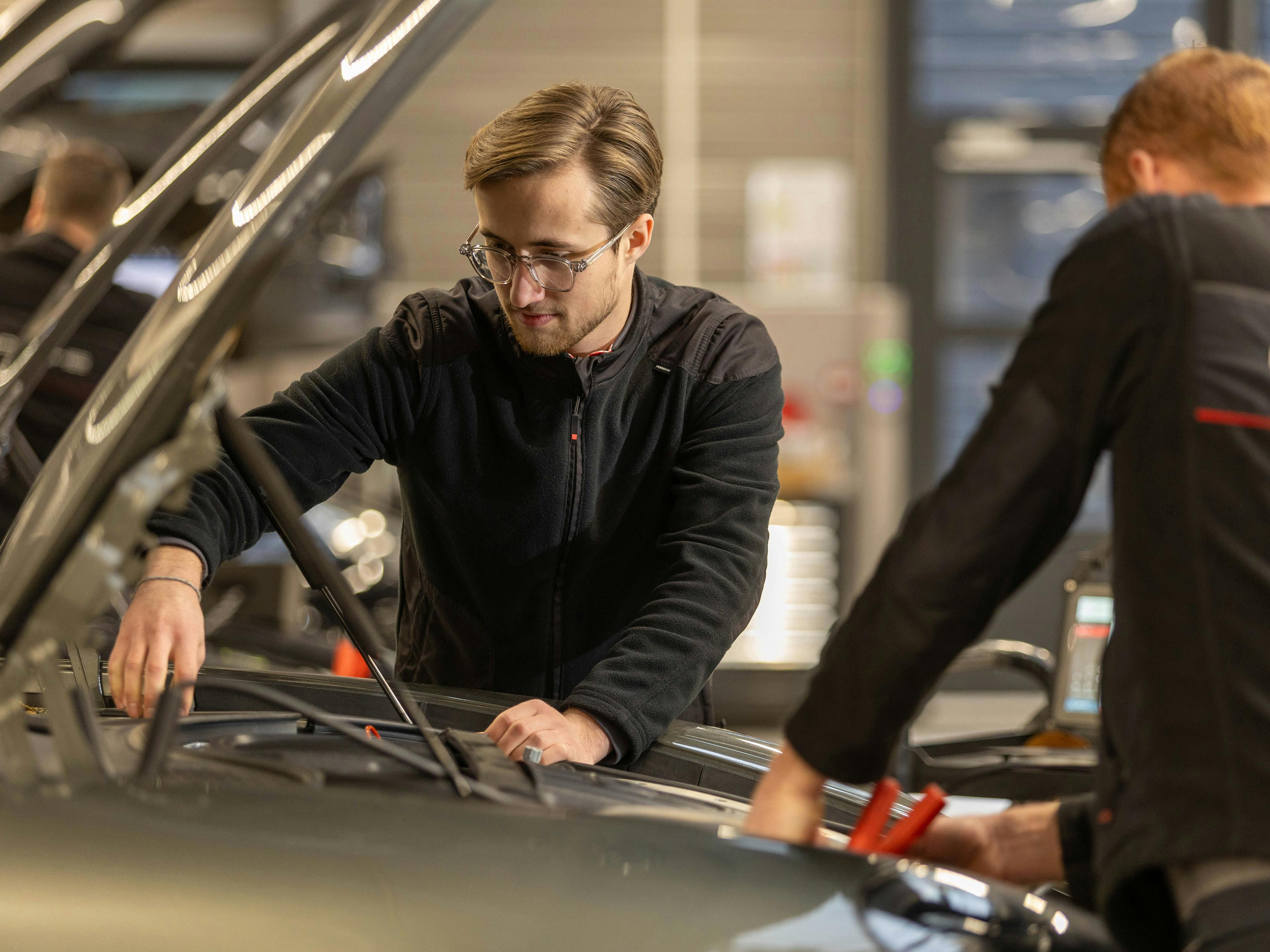 Deux techniciens Porsche travaillent sous le capot d'un véhicule Porsche.