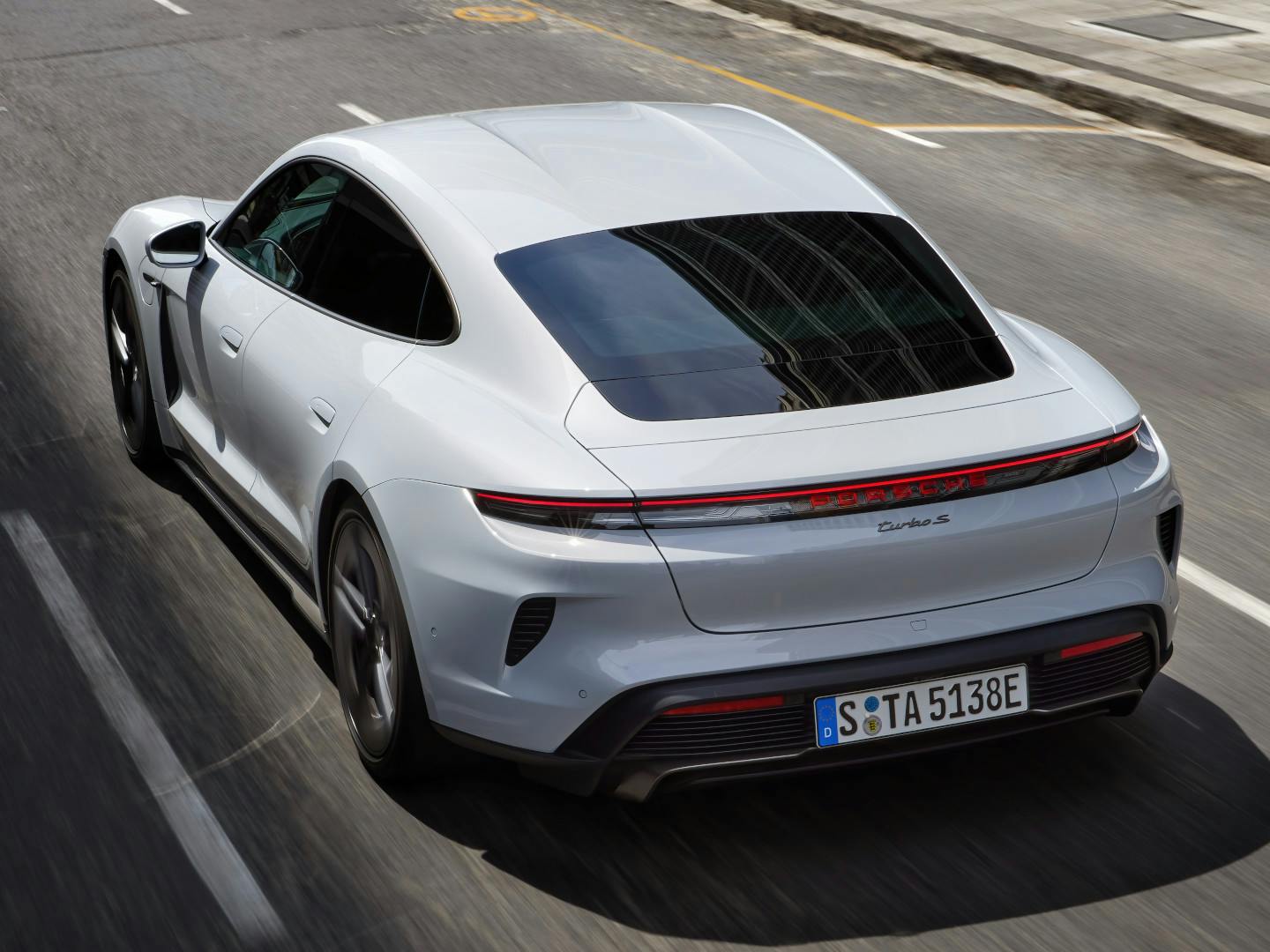 A white Porsche Taycan Turbo S driving on a road.