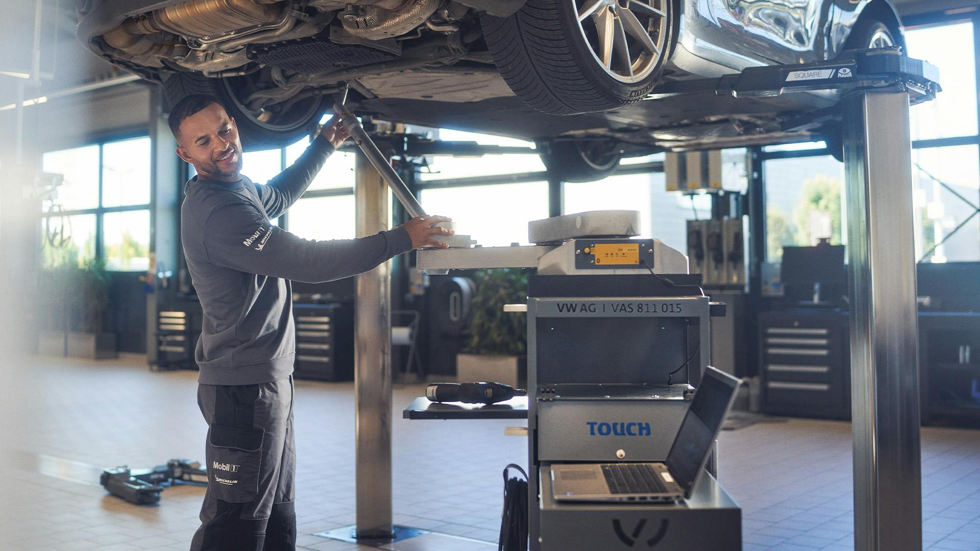 Un mecánico de Porsche trabajando debajo de un vehículo elevado. Vista detallada de los bajos y las llantas de un modelo Porsche.
