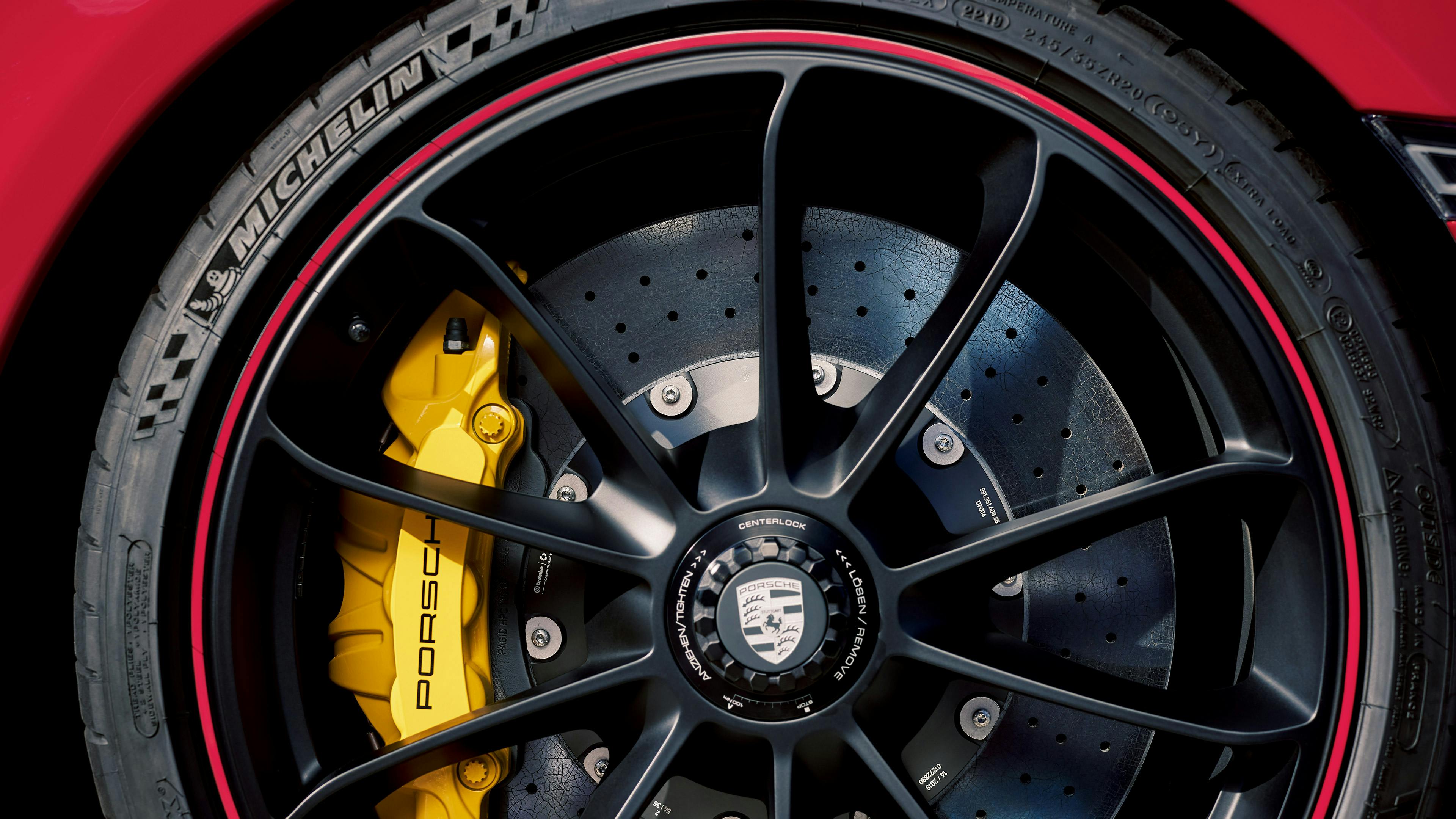 Nahaufnahme eines Porsche-Rads mit gelben Bremssätteln, schwarzer Felge und Michelin Reifen. Sichtbare Bremsscheibe und Porsche-Logo in Zentrum.