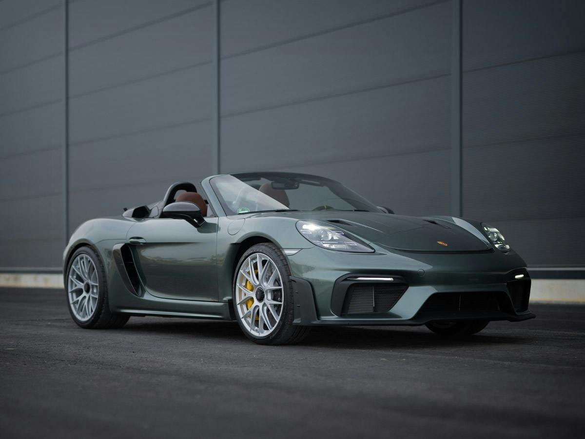 A 718 Spyder RS coloured in Malachitegreenmetalic with cabriolet open from the front in front of a building.