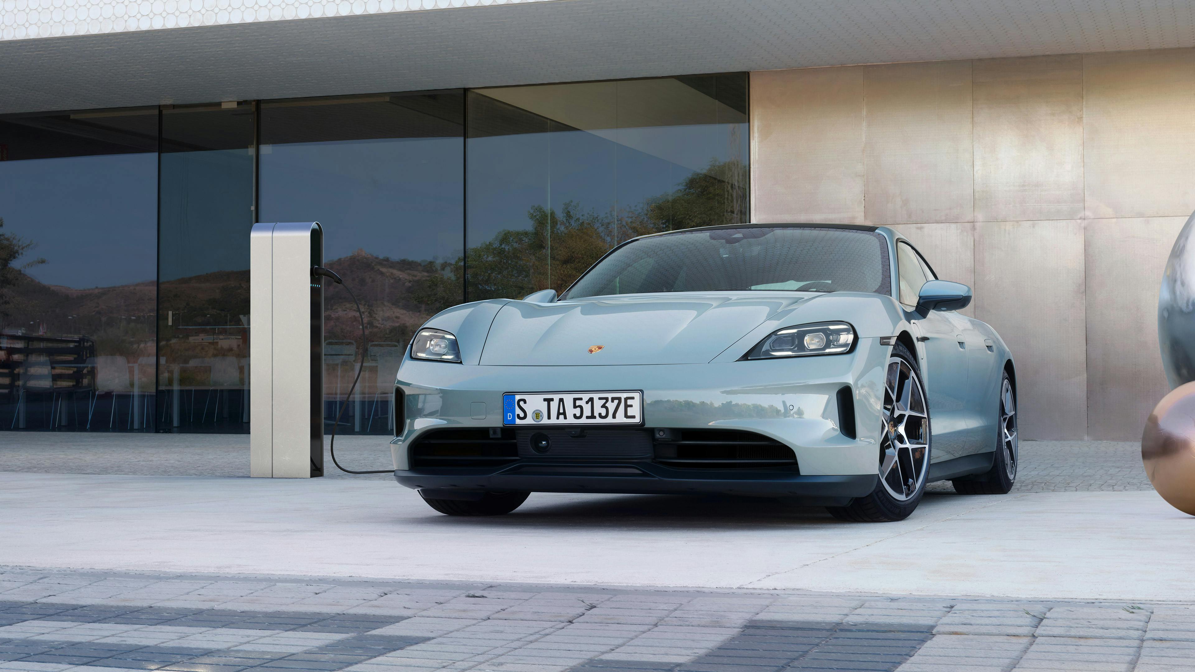 Un Porsche Taycan bleu clair en branché sur une station de recharge.