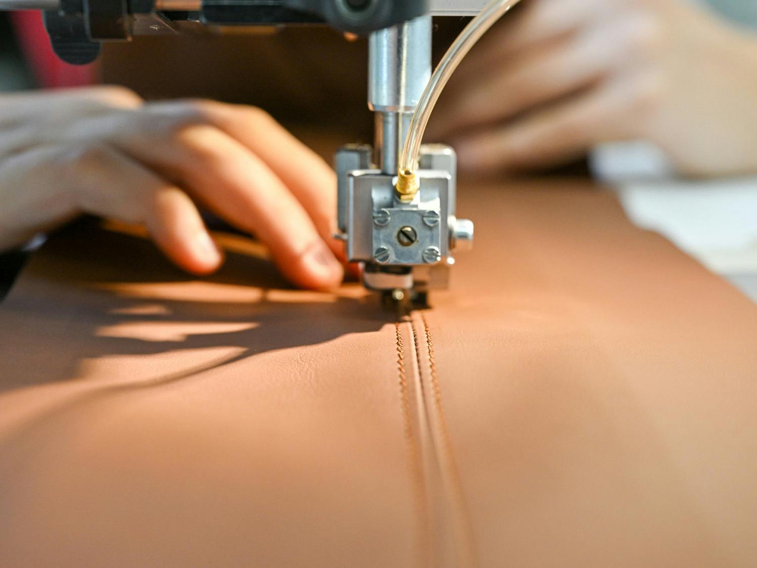 Person sewing a piece of brown leather.