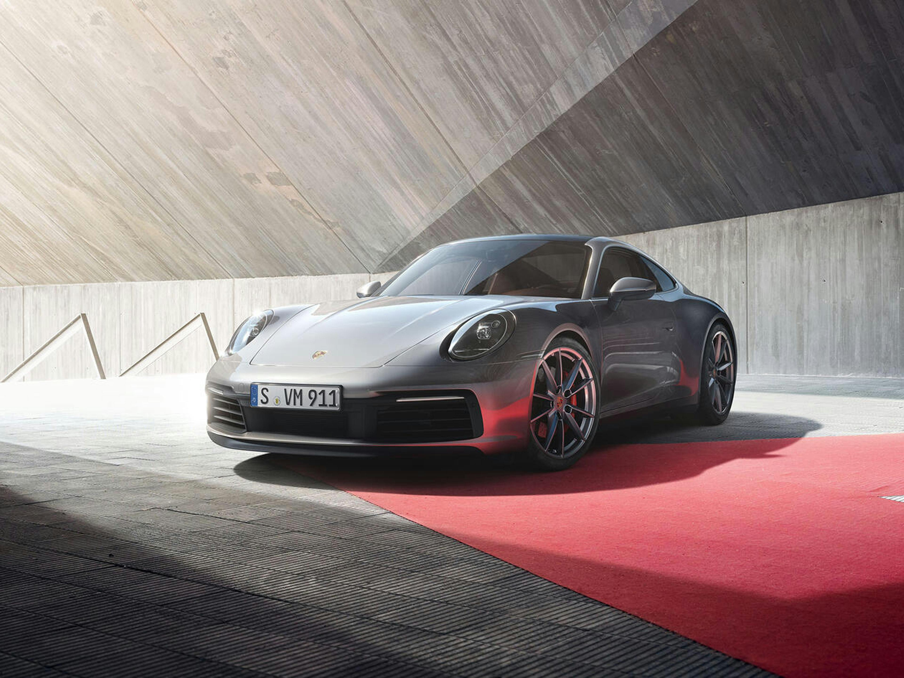Ein Porsche 911 steht auf einem roten Teppich vor moderner Betonarchitektur.