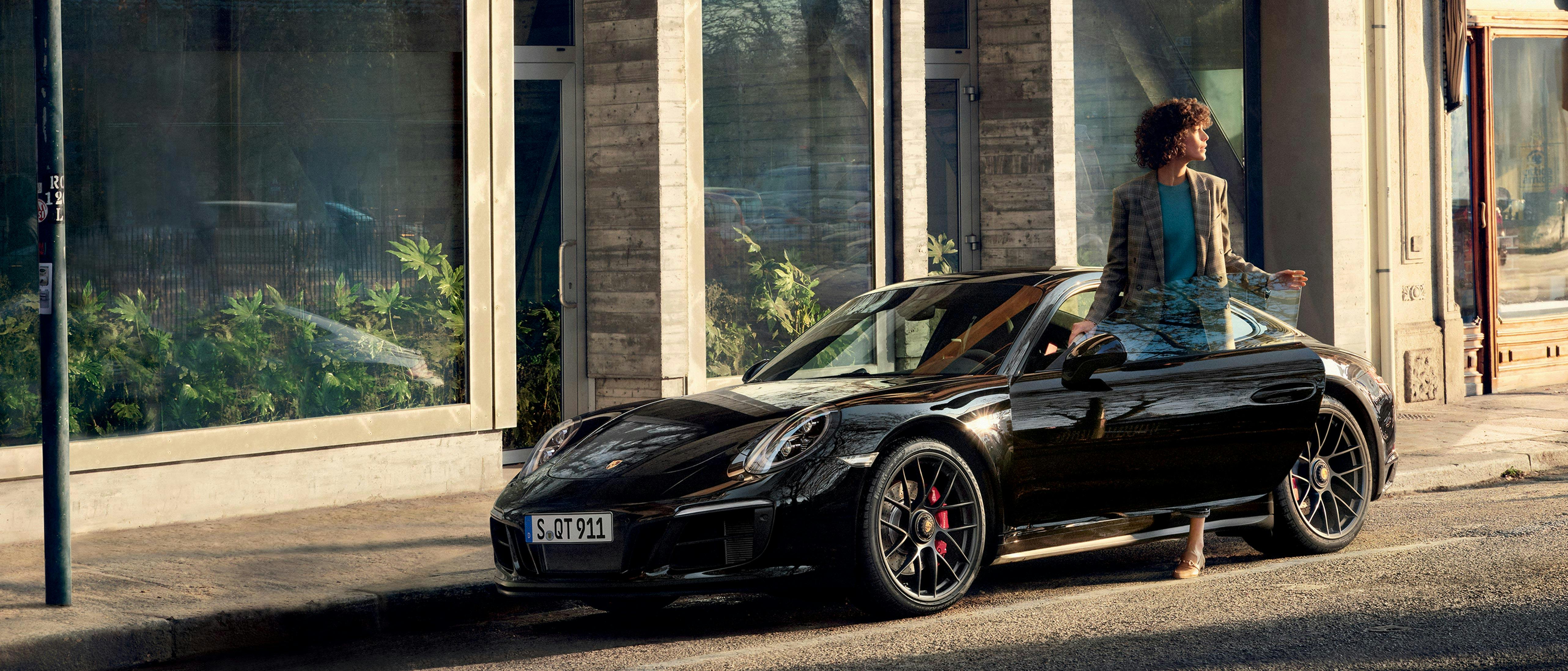 Young woman stepping out of a black Porsche 911 in an urban environment.