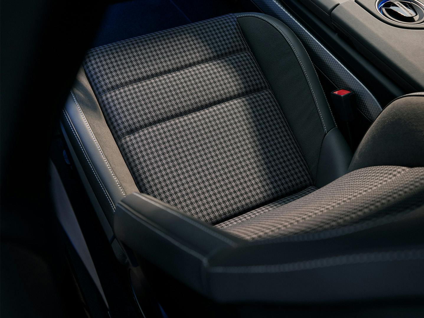 Close-up of a Porsche car seat featuring a houndstooth-patterned fabric in the center, surrounded by black leather with visible white stitching, showcasing a blend of classic and modern design elements.