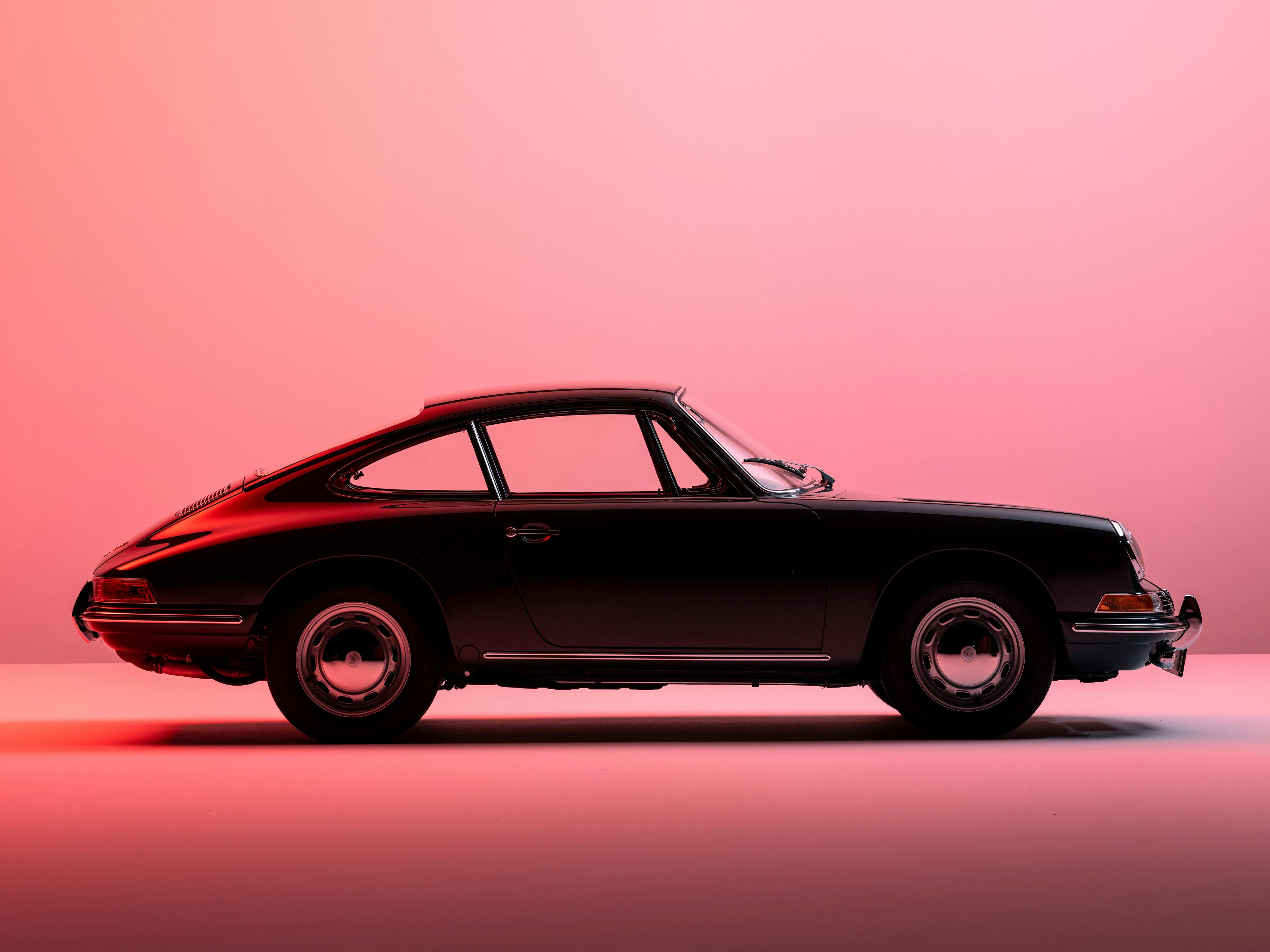 Seitenansicht eines klassischen schwarzen Porsche 911 vor einem rosa Hintergrund, der die ikonische Silhouette des Autos betont.