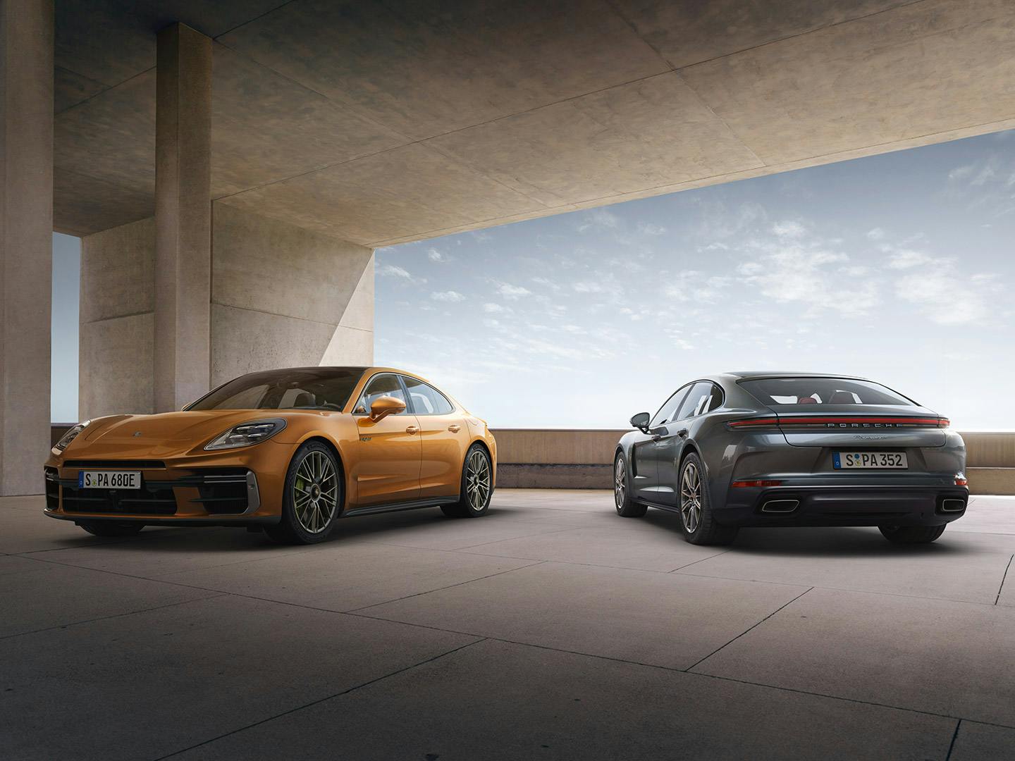 Une Panamera orange et une Panamera grise stationnées côte à côte sous un pont.