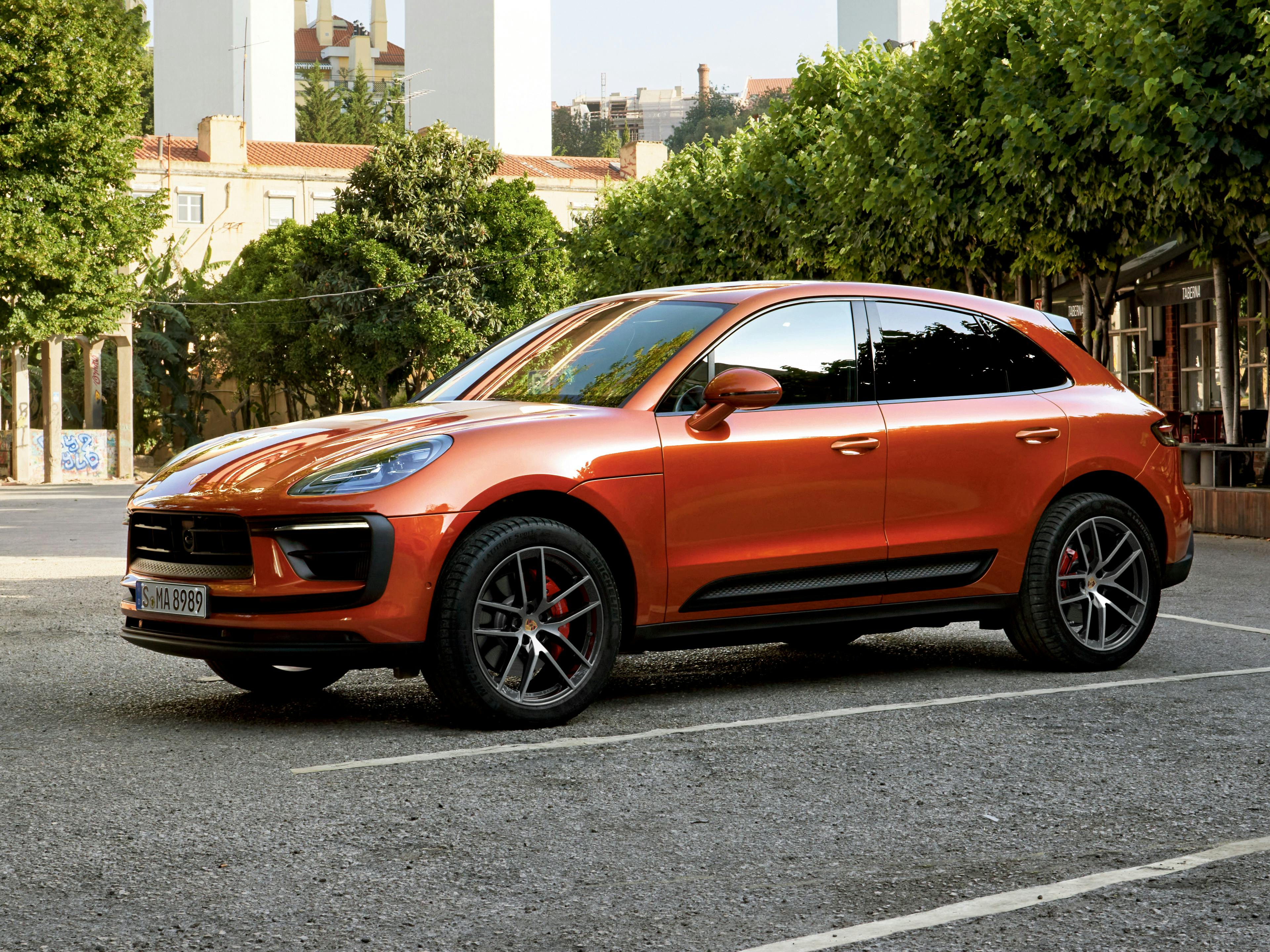 The Macan S in white lined parking bay, with trees and building visible in the background.