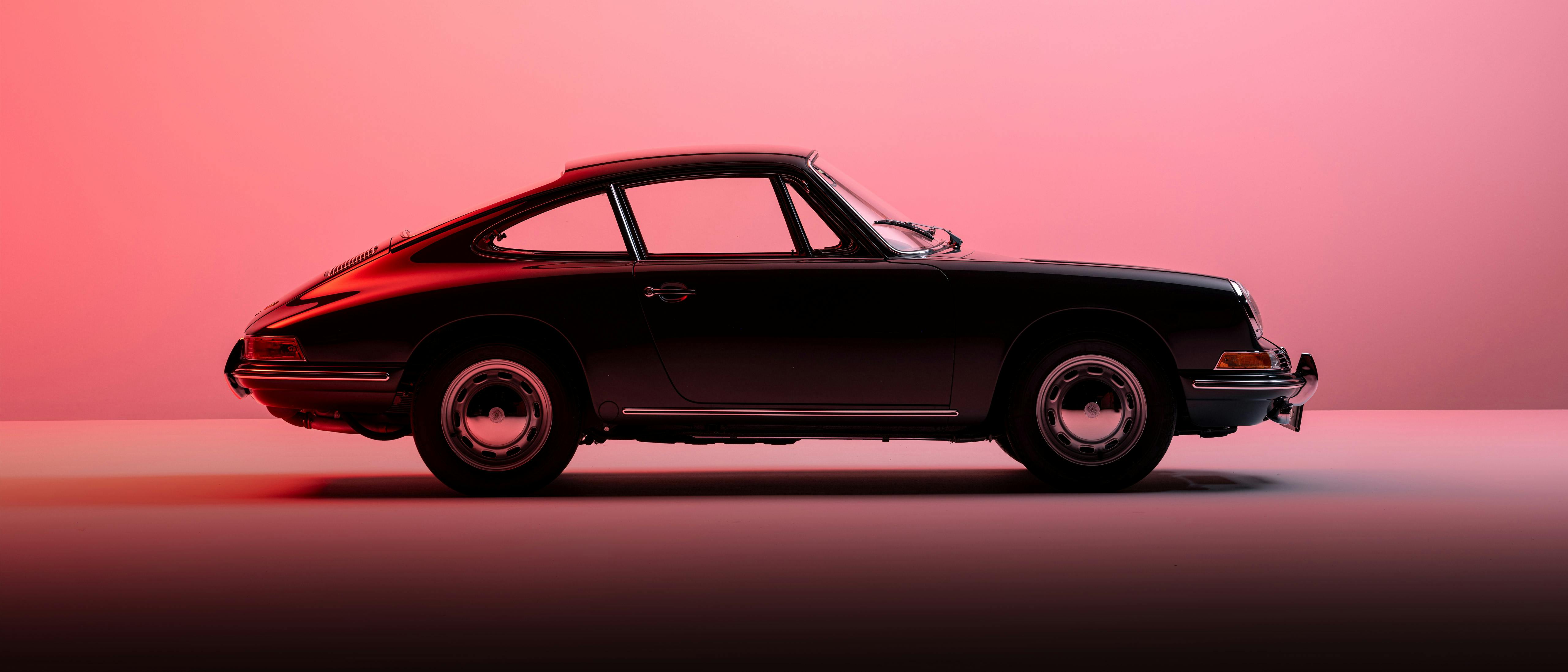 Seitenansicht eines klassischen schwarzen Porsche 911 vor einem rosa Hintergrund, der die ikonische Silhouette des Autos betont.